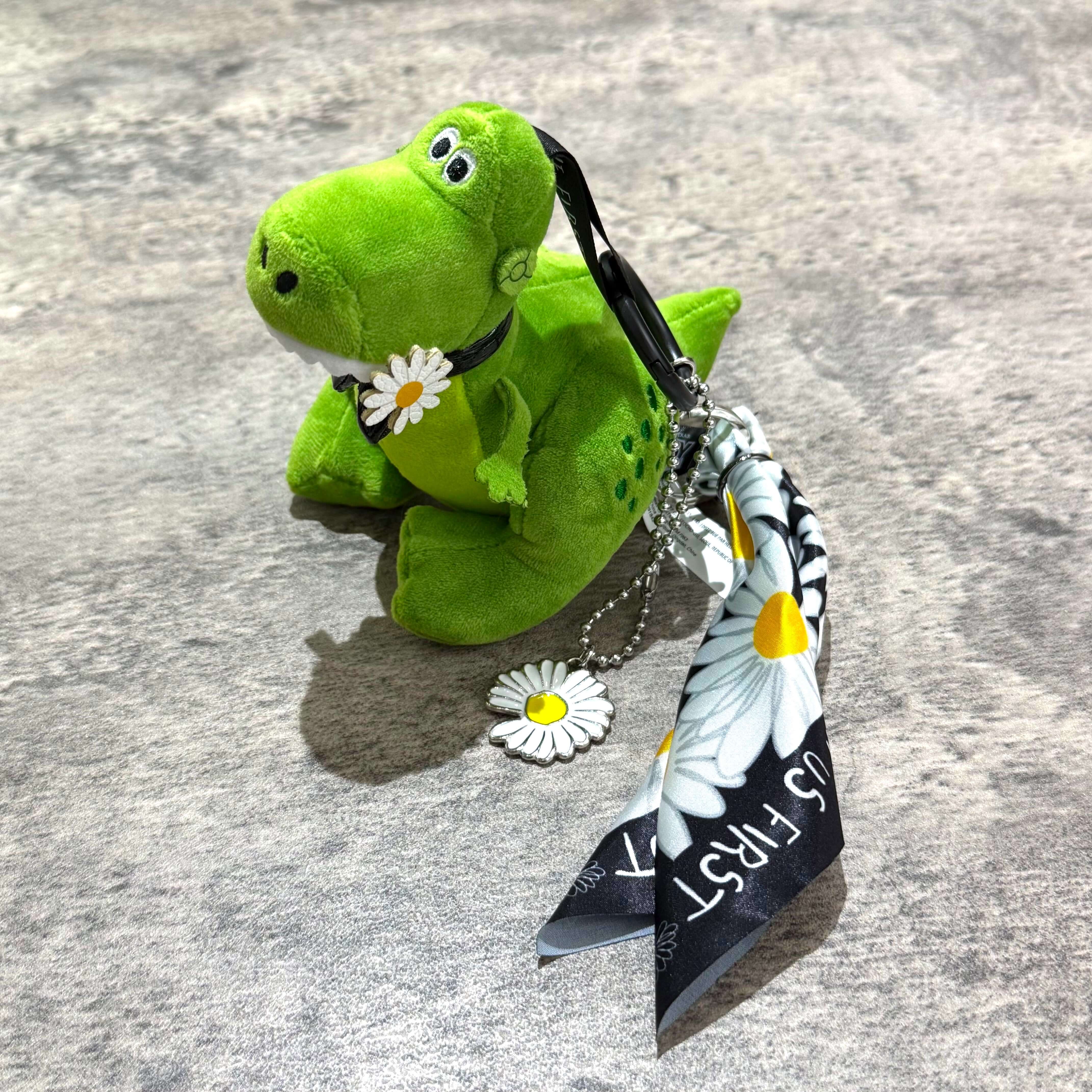 PEACEMINUSONE x Toy Story The First Fan - Plush Keyring 盲盒已開的綠色毛絨恐龍公仔,附帶花朵飾品和絲帶。