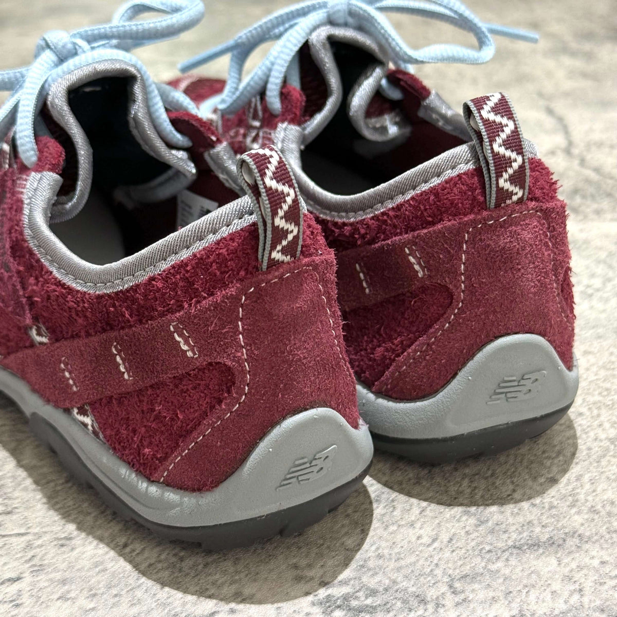 SUNLOVETOUR x New Balance MT1001ND showing the back view of rugged shoes with maroon and gray details.