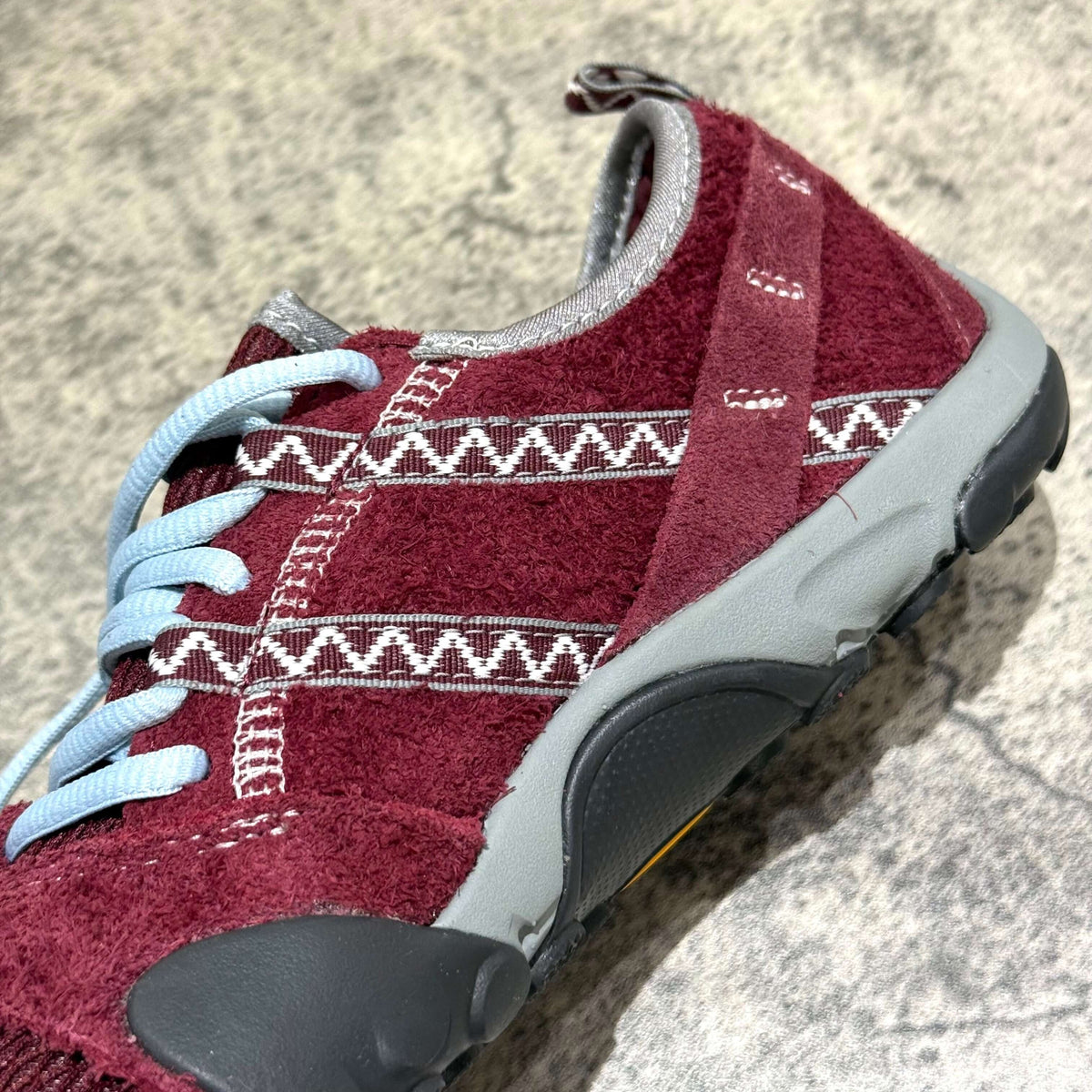 Close-up of SUNLOVETOUR x New Balance MT1001ND shoe showcasing maroon color and textured design elements.
