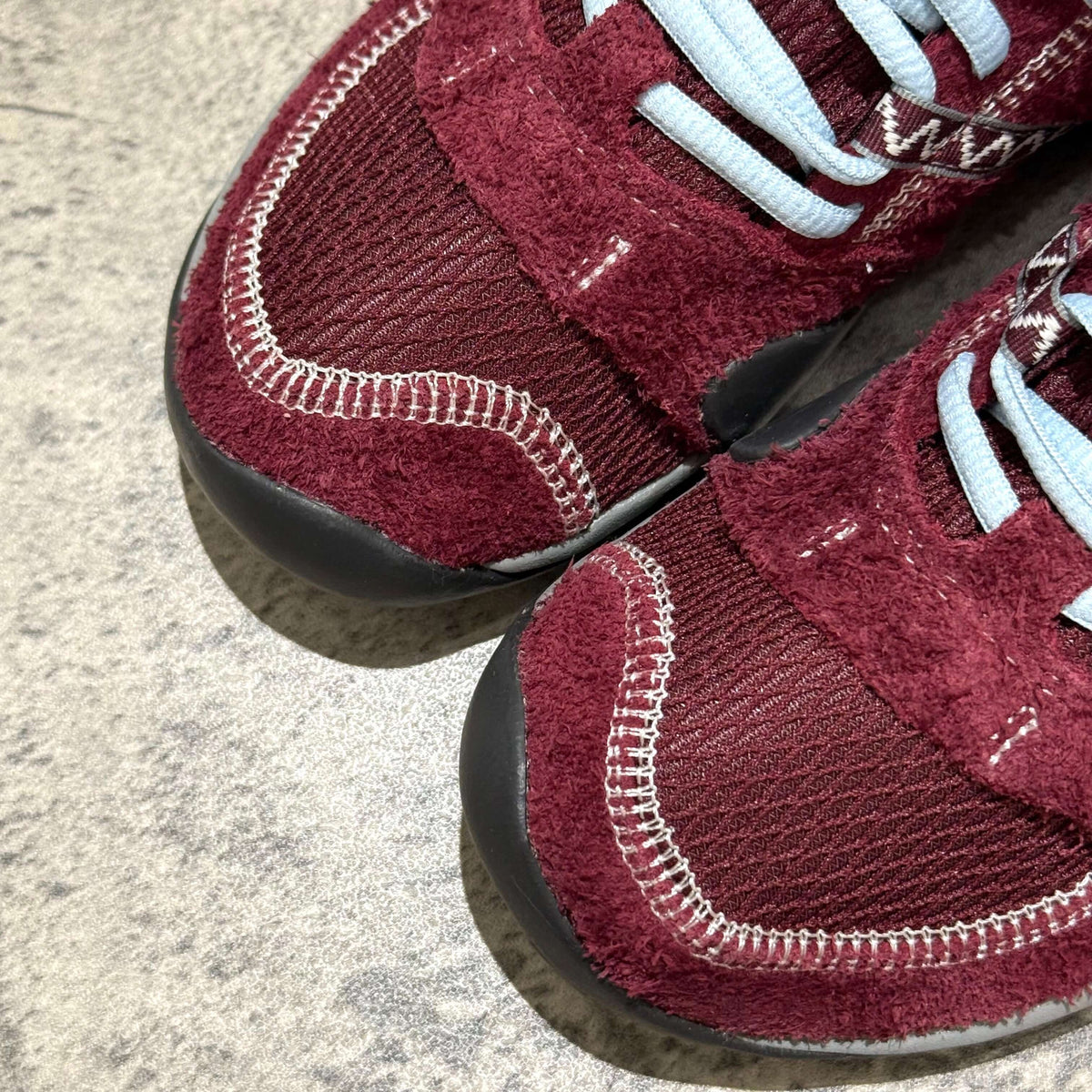 Close-up of SUNLOVETOUR x New Balance MT1001ND sneakers showing maroon color and texture details.