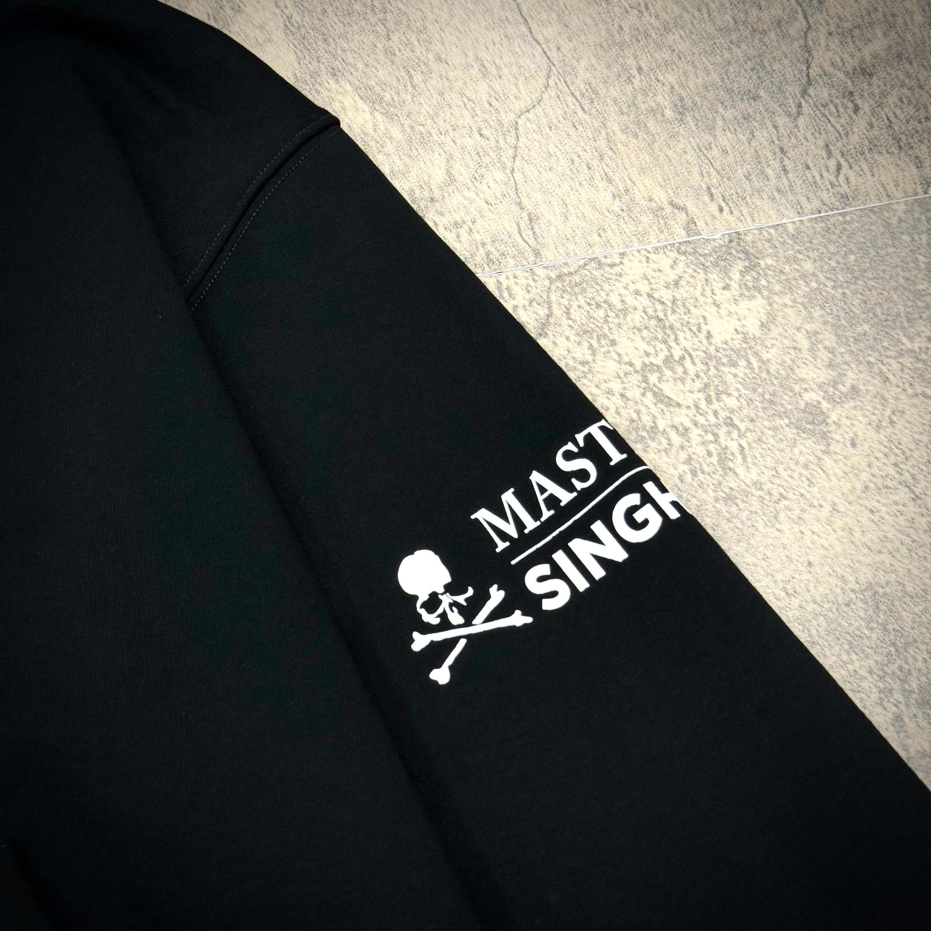 Close-up of the Singha Soda x Mastermind World Zip Up Hoodie showcasing the iconic Mastermind logo on the sleeve.