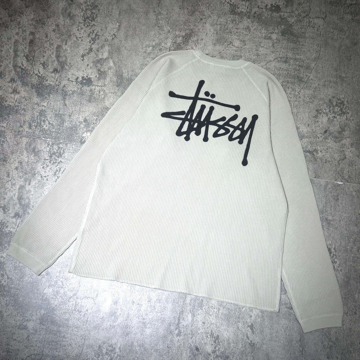 Stussy Basic Raglan Thermal LS Crew FW26 in cream color with black logo on the back, casual long sleeve designed for comfort.