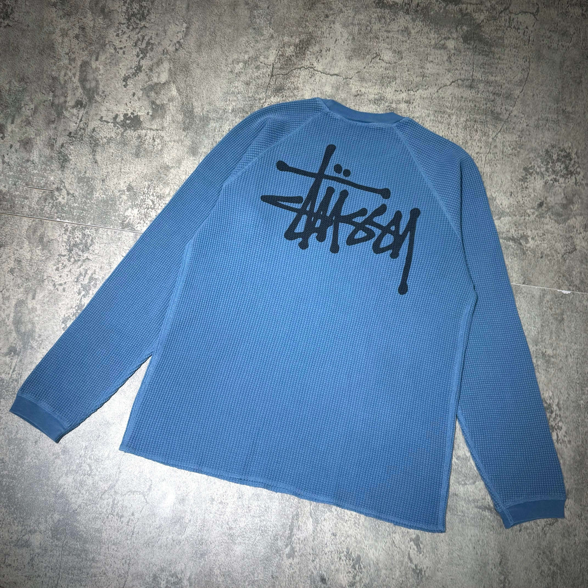 Stussy Basic Raglan Thermal LS Crew FW26 in blue, featuring a black logo on the back, showcasing a stylish casual design.