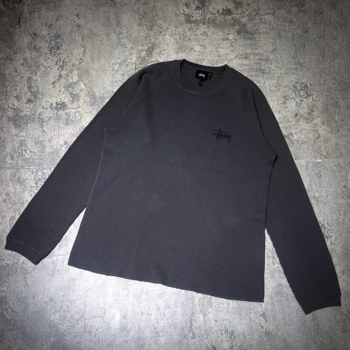 Stussy Basic Raglan Thermal LS Crew FW26 in dark grey, showcasing ribbed texture and embroidered logo on chest.