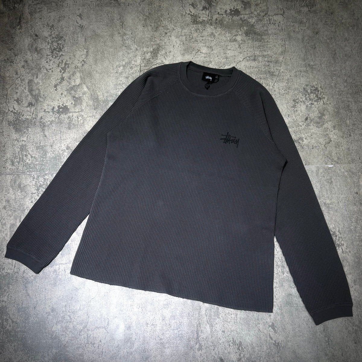 Stussy Basic Raglan Thermal LS Crew FW26 in dark grey, showcasing ribbed texture and embroidered logo on chest.