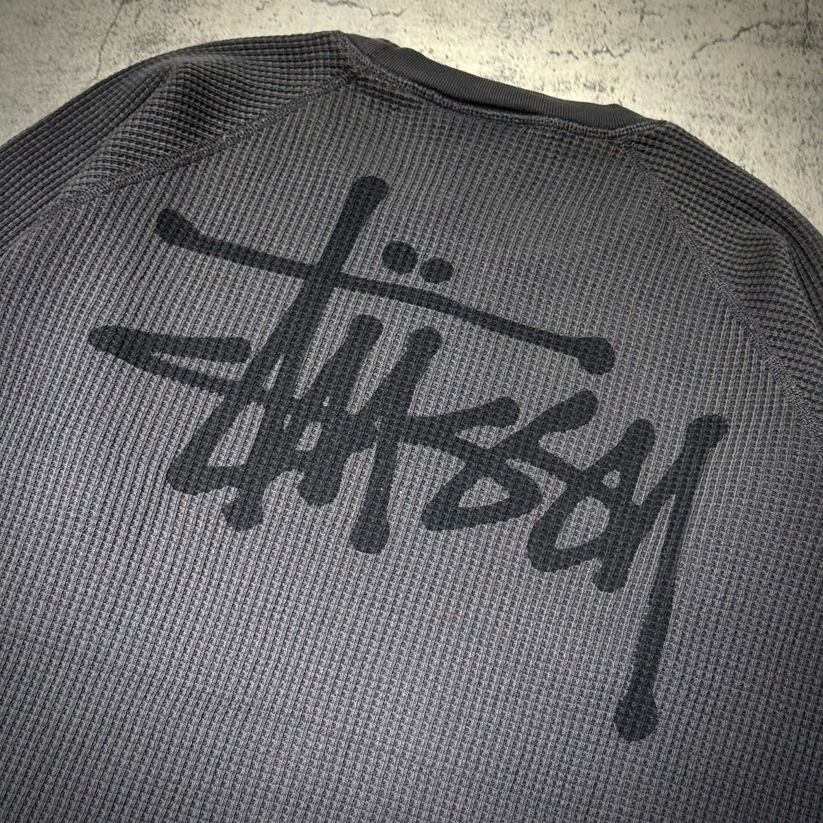Stussy Basic Raglan Thermal LS Crew FW26 with iconic Stussy logo on the back, textured grey fabric design.