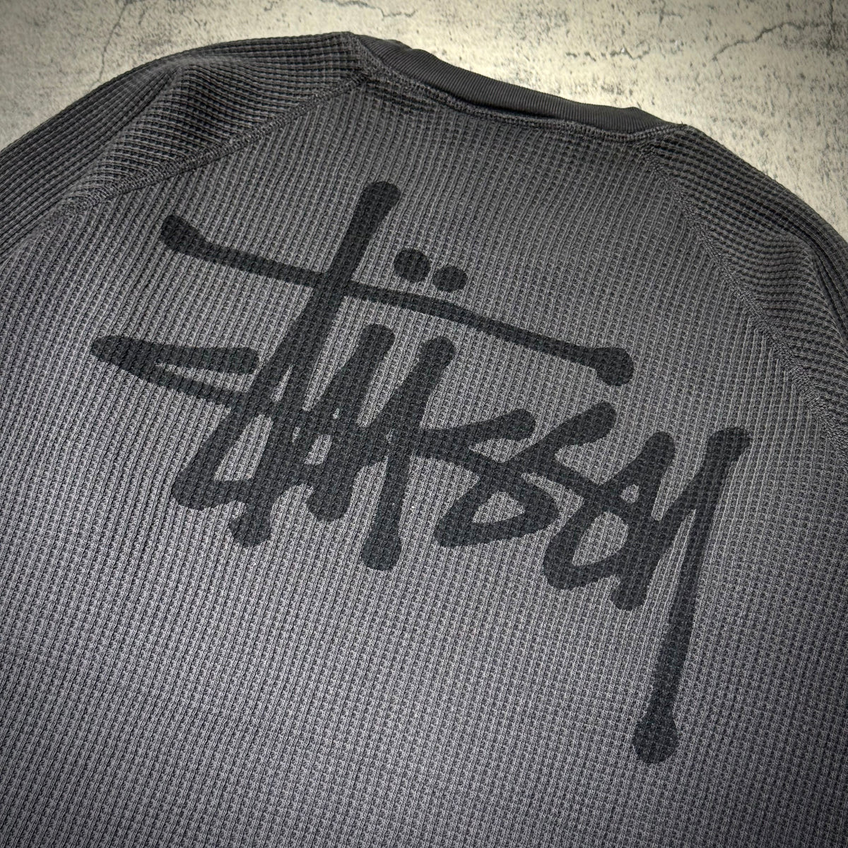 Stussy Basic Raglan Thermal LS Crew FW26 with iconic Stussy logo on the back, textured grey fabric design.