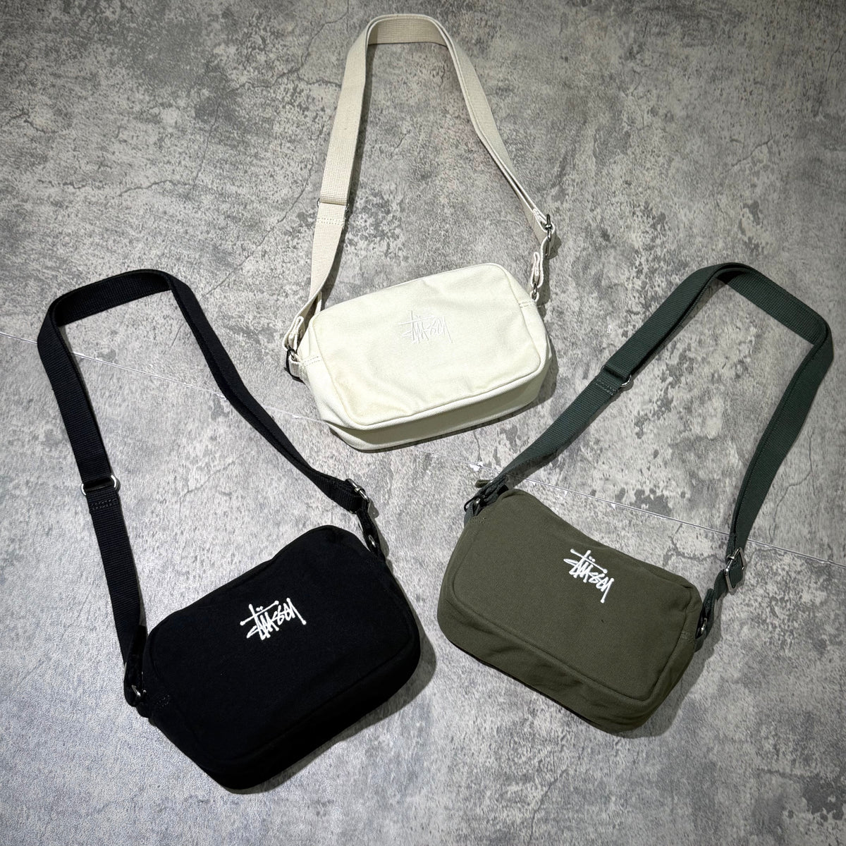 Stussy Canvas Side Pouch in black, white, and green displayed on a textured surface.