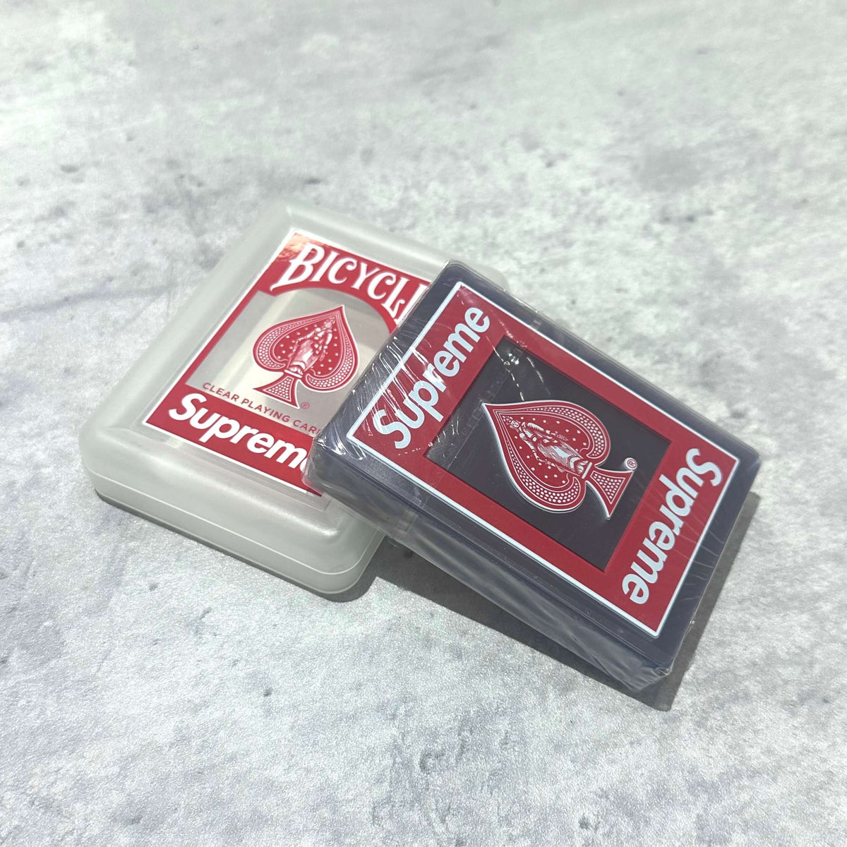 Supreme Bicycle Clear Playing Cards Red packaging displayed on a gray surface.