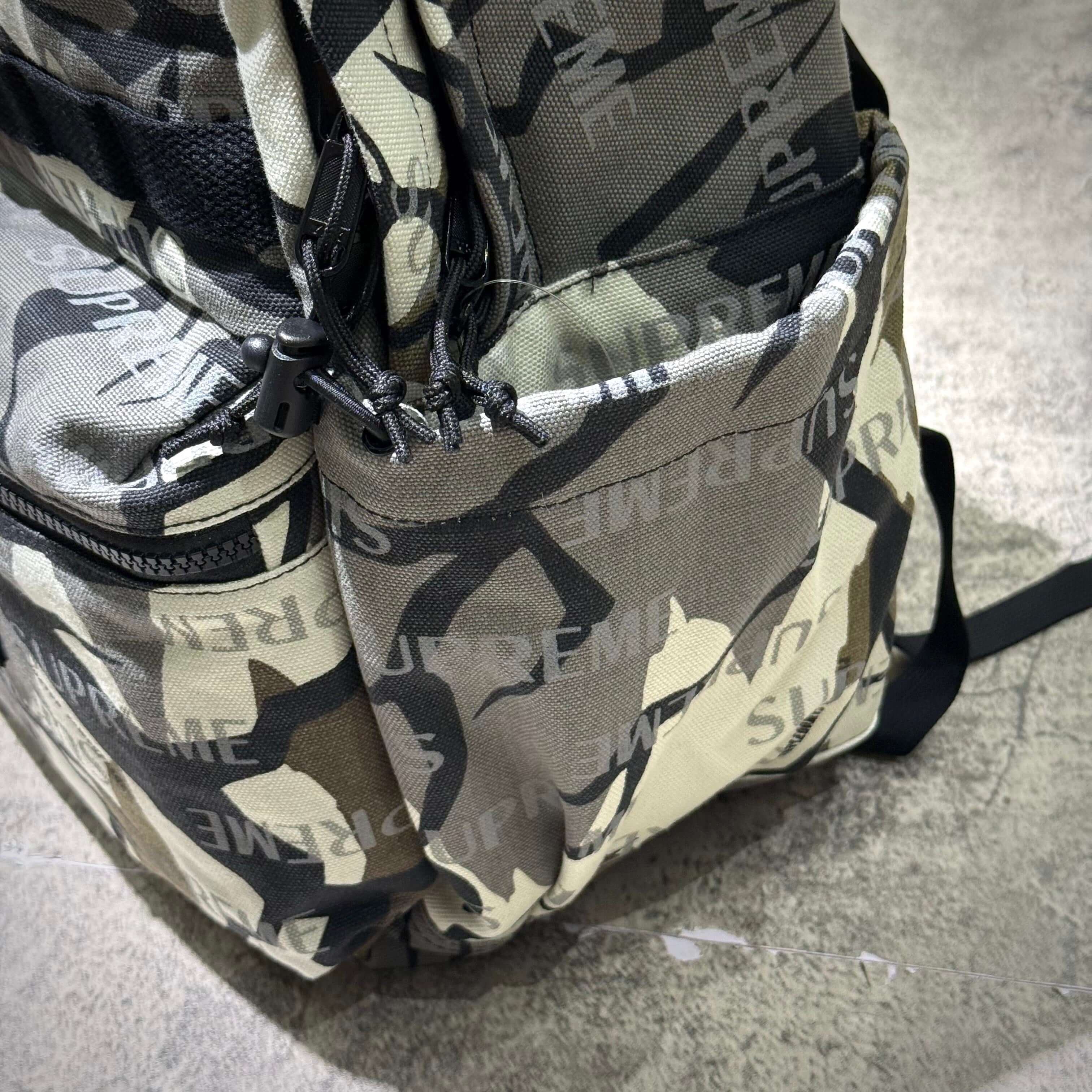 Close-up of Supreme FW26 Backpack featuring camouflage pattern and distinct branding details.