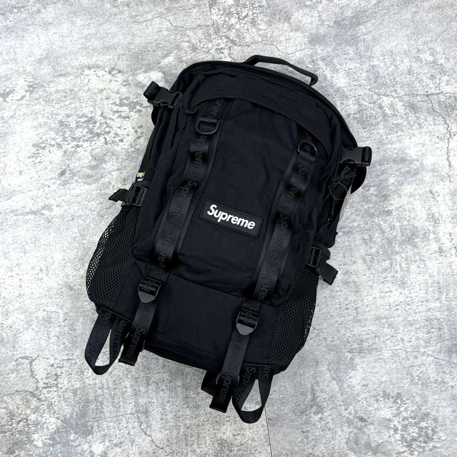 Supreme Backpack SS26, a black water-resistant backpack with multiple straps and mesh pockets.