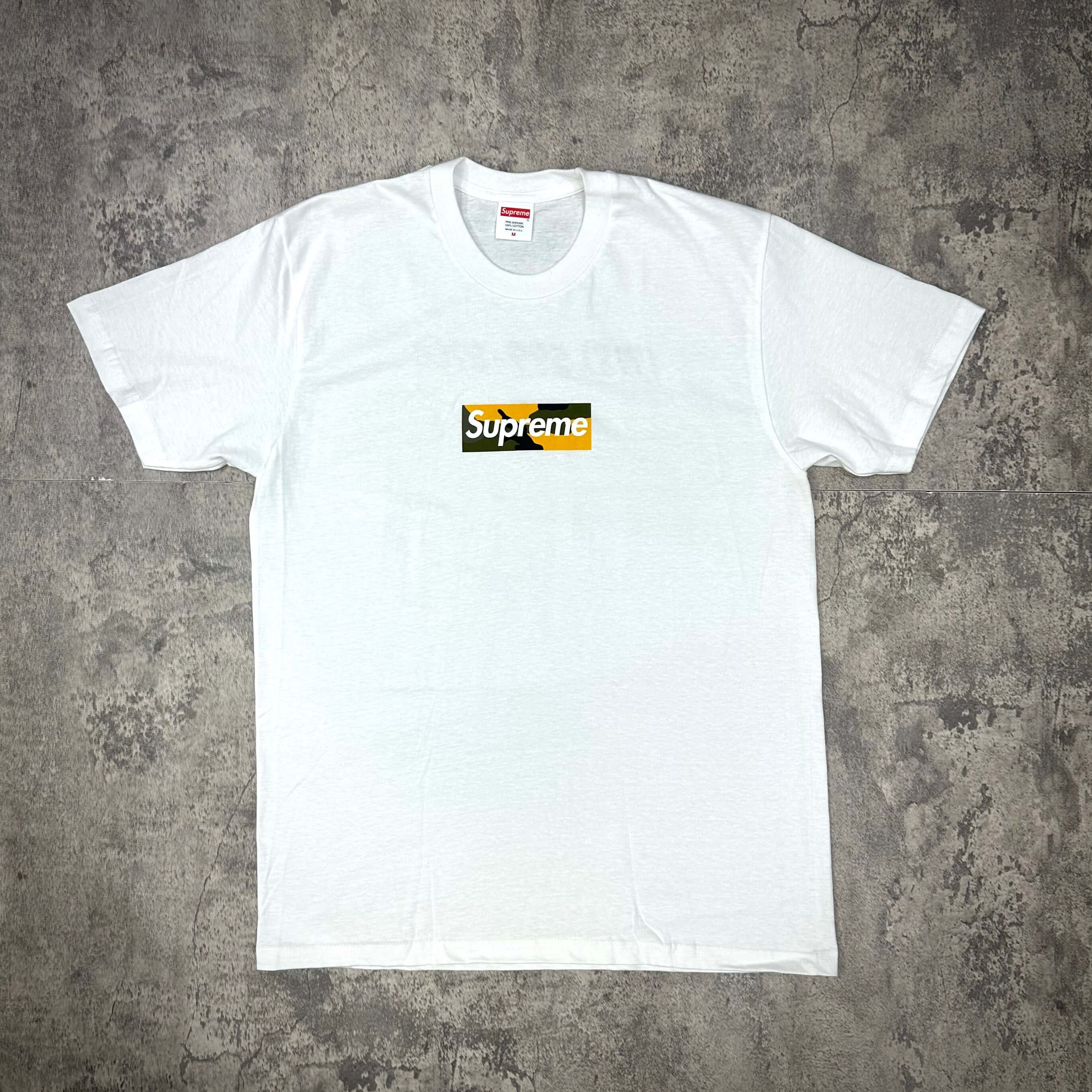 Supreme Brooklyn Box Logo Tee - White displayed on a gray surface, showcasing the classic design and fit.