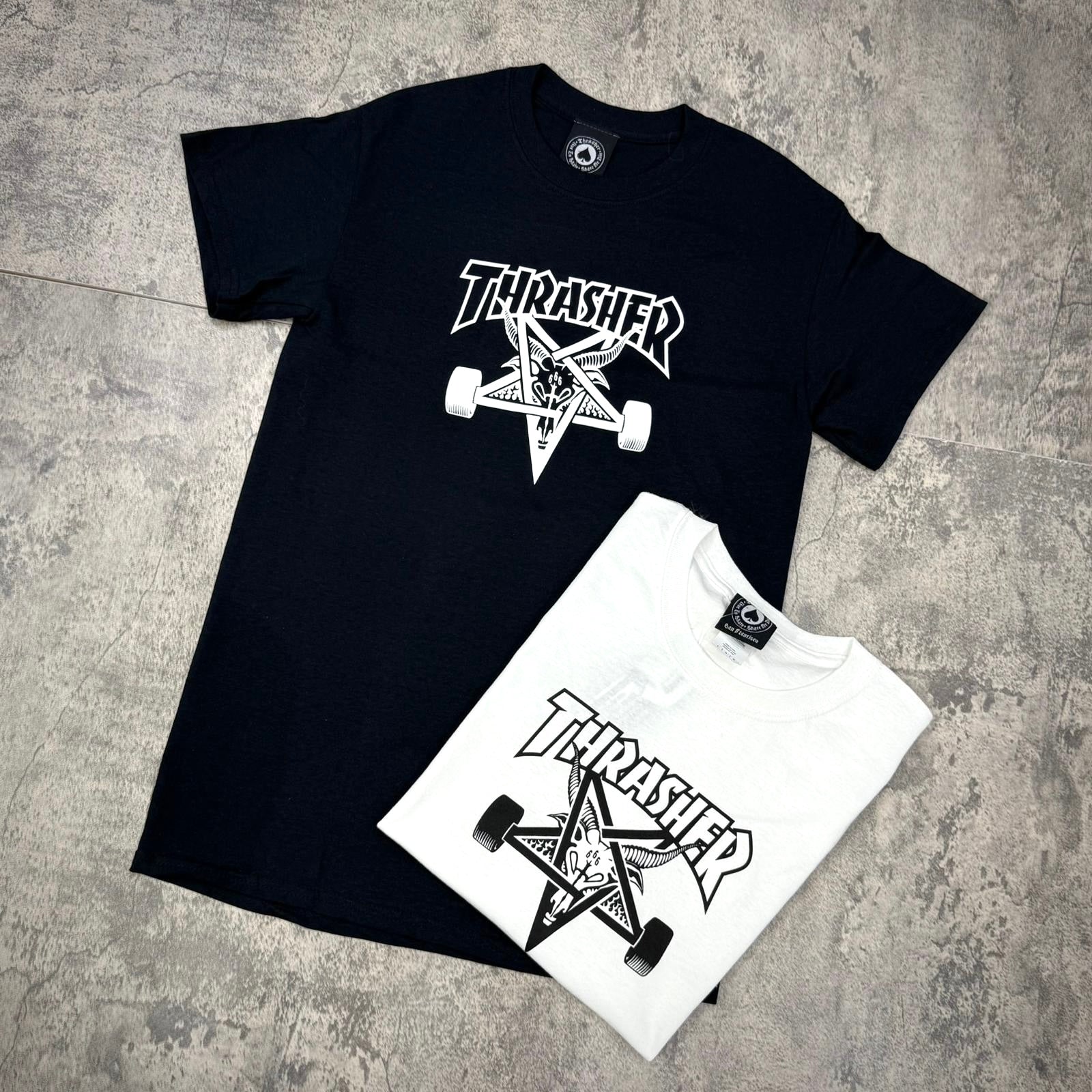 Thrasher Skate Goat Tee - Black / White t-shirts laid on a textured surface, showcasing iconic Thrasher logo design.