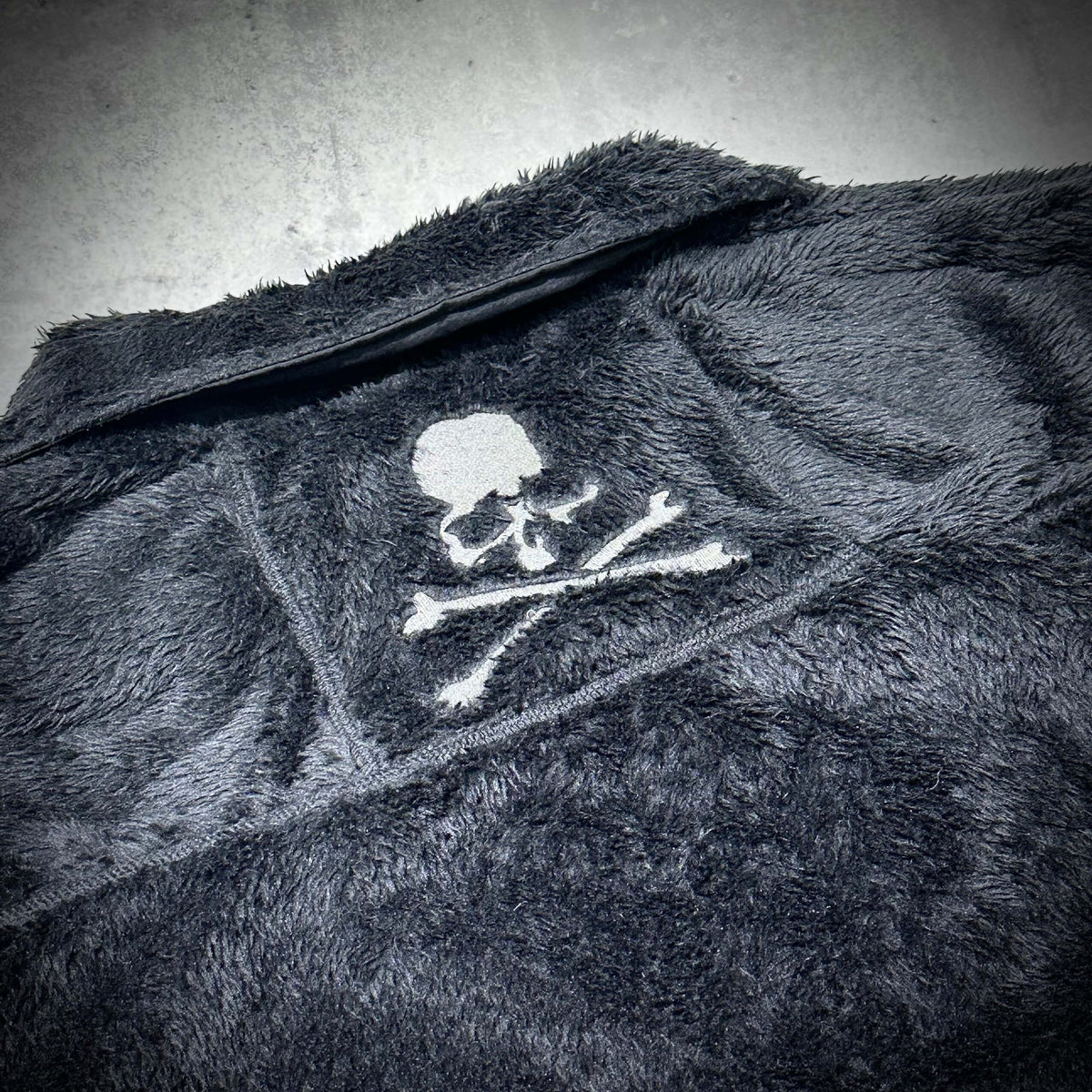 Wild Things x Mastermind World Shaggy Zip Up Jacket featuring a skull and crossbones design on a soft fabric.