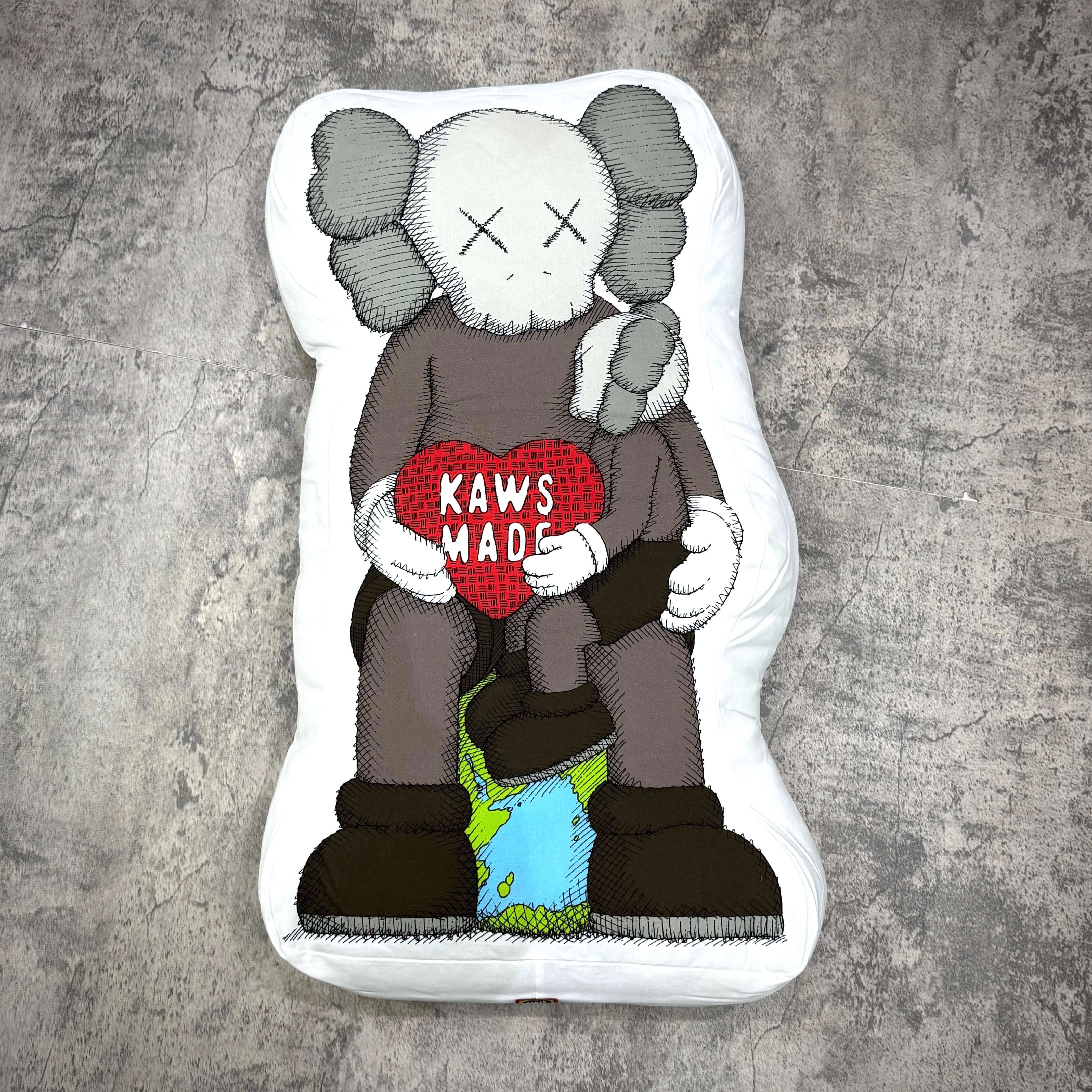Human Made Bangkok Exclusive Kaws Made Cushion featuring Kaws character holding a heart-shaped 'KAWS MADE' cushion.