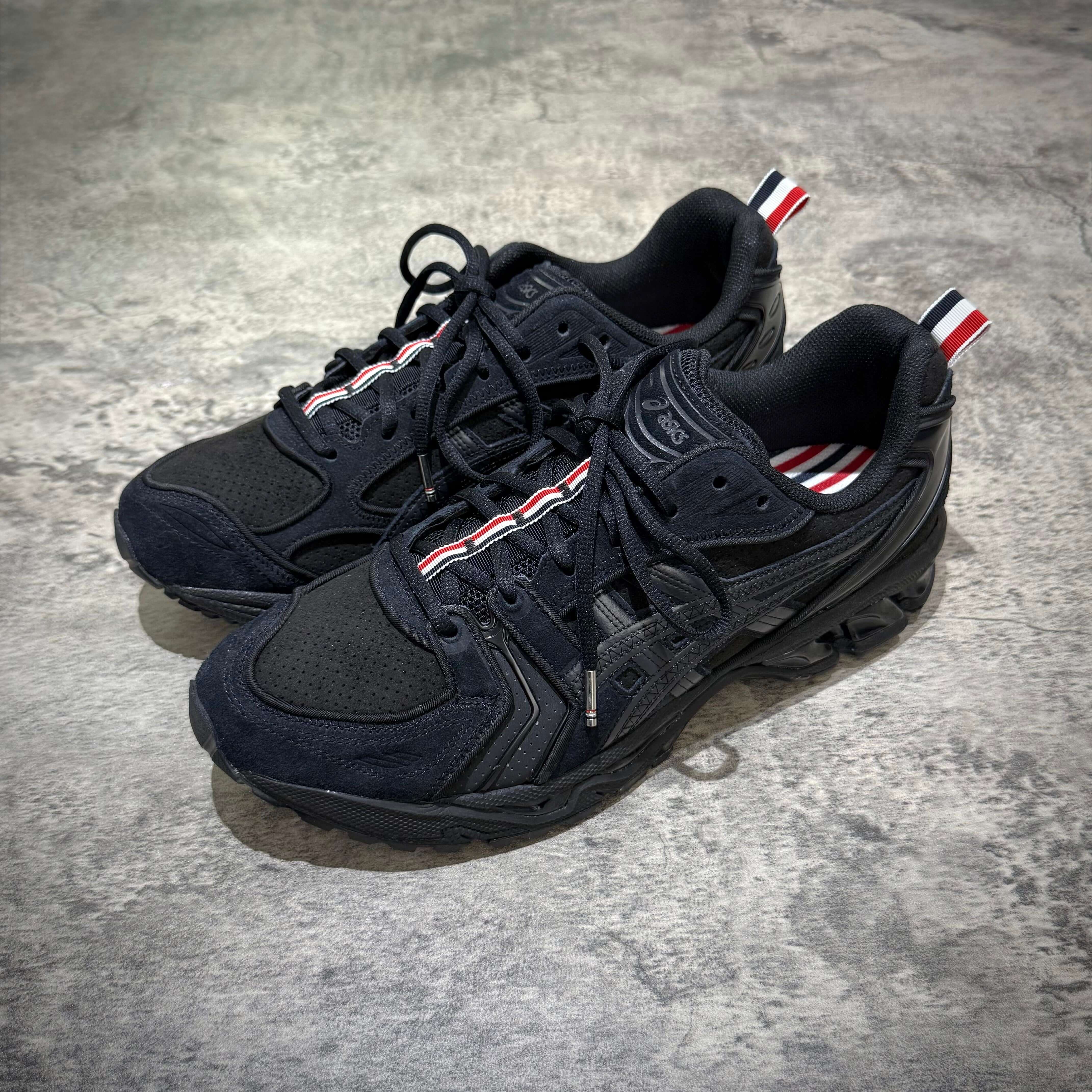 Thom Browne x Asics Gel-Kayano 14 in Black, featuring a sleek design and signature stripes for stylish athletic wear.