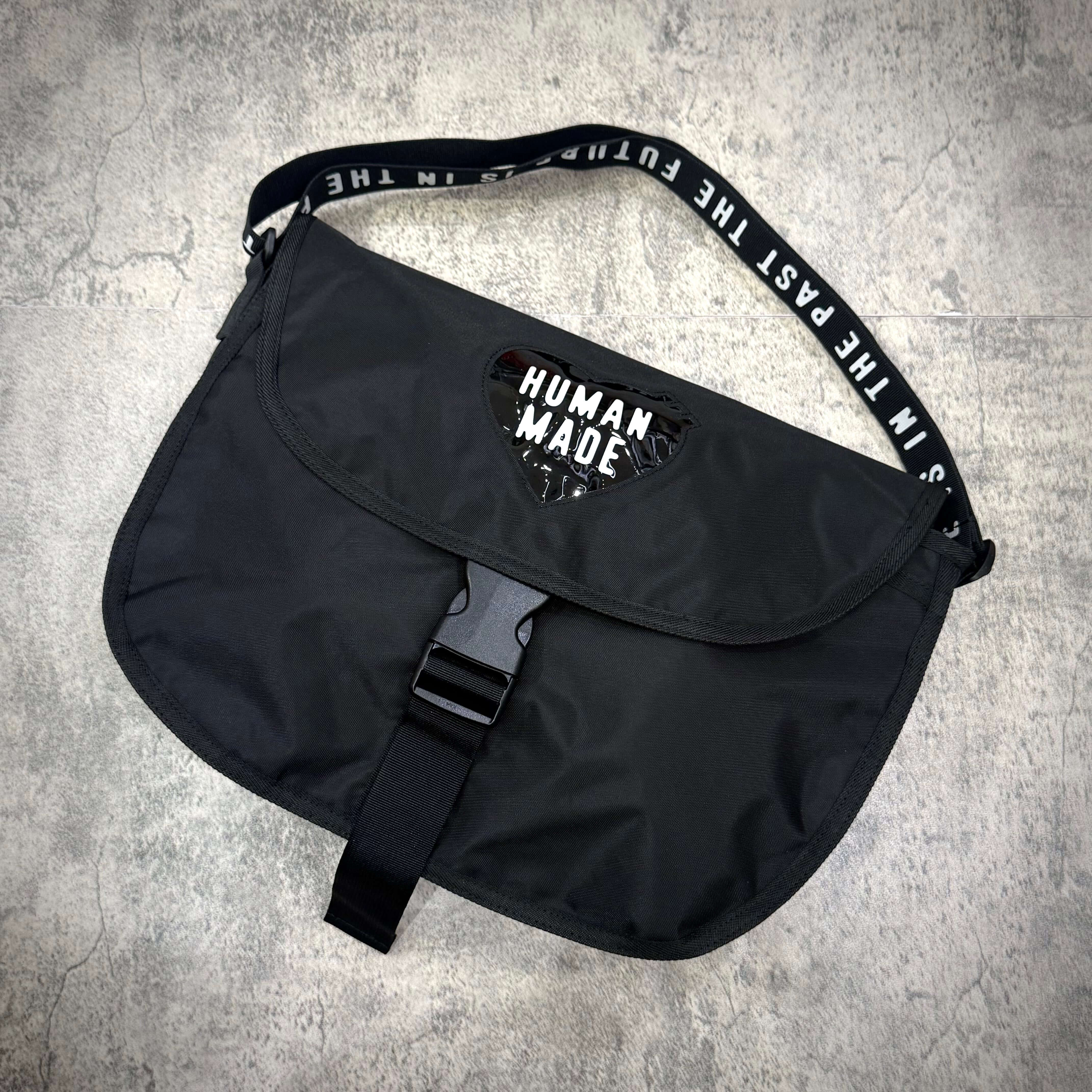 Human Made Nylon Shoulder Bag featuring a sleek black design and adjustable strap on a textured surface.