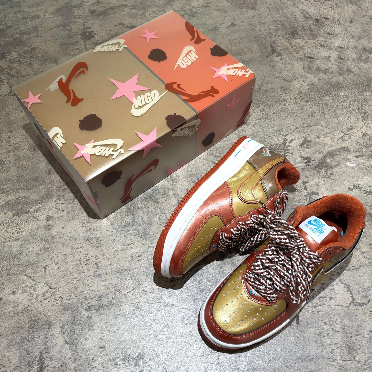 01 x Nigo x J-HOPE Nike Air Force 1 IO8766-800 in gold and brown with unique packaging.