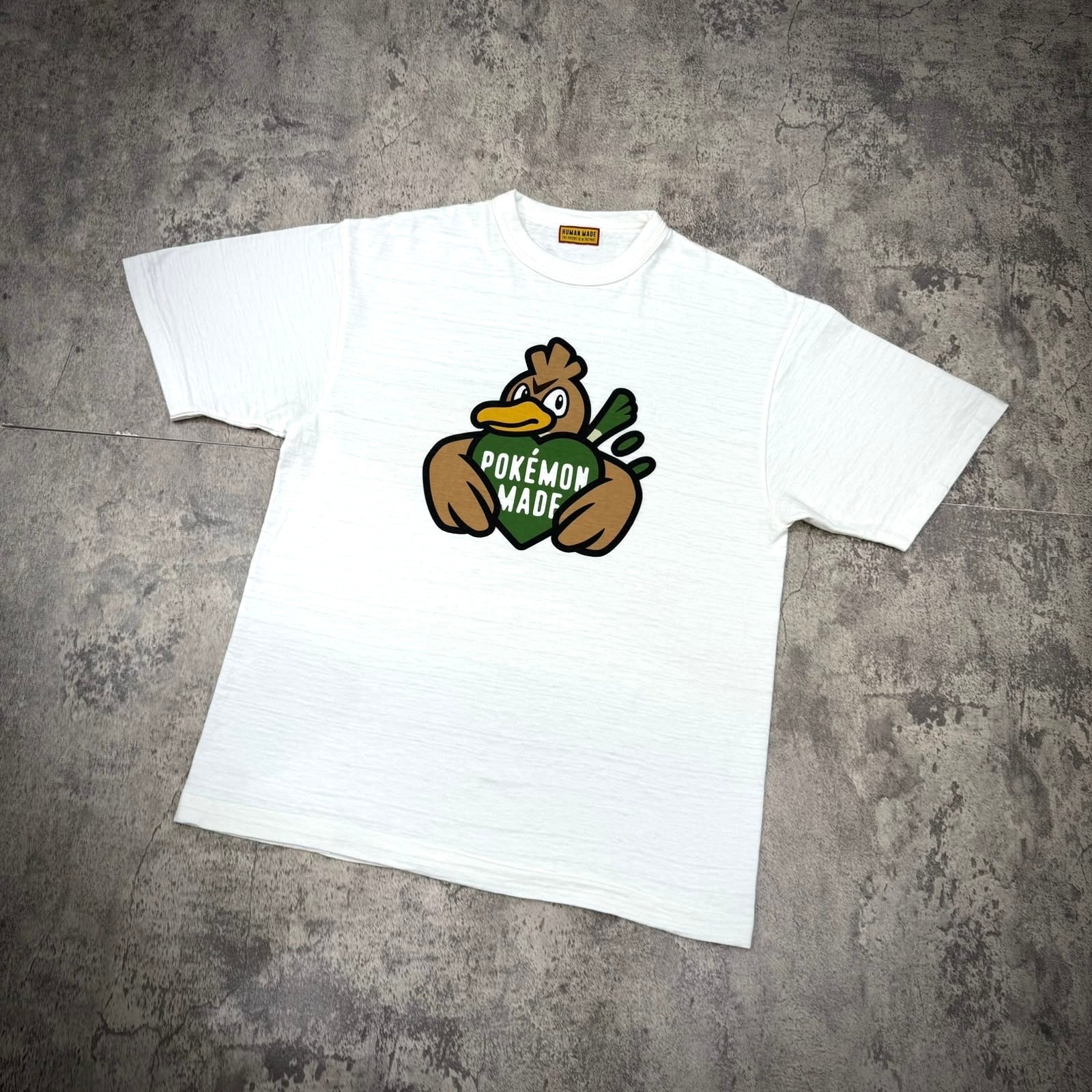 Human Made x Pokemon graphic tee featuring a duck holding a green heart with 'POKEMON MADE' text.