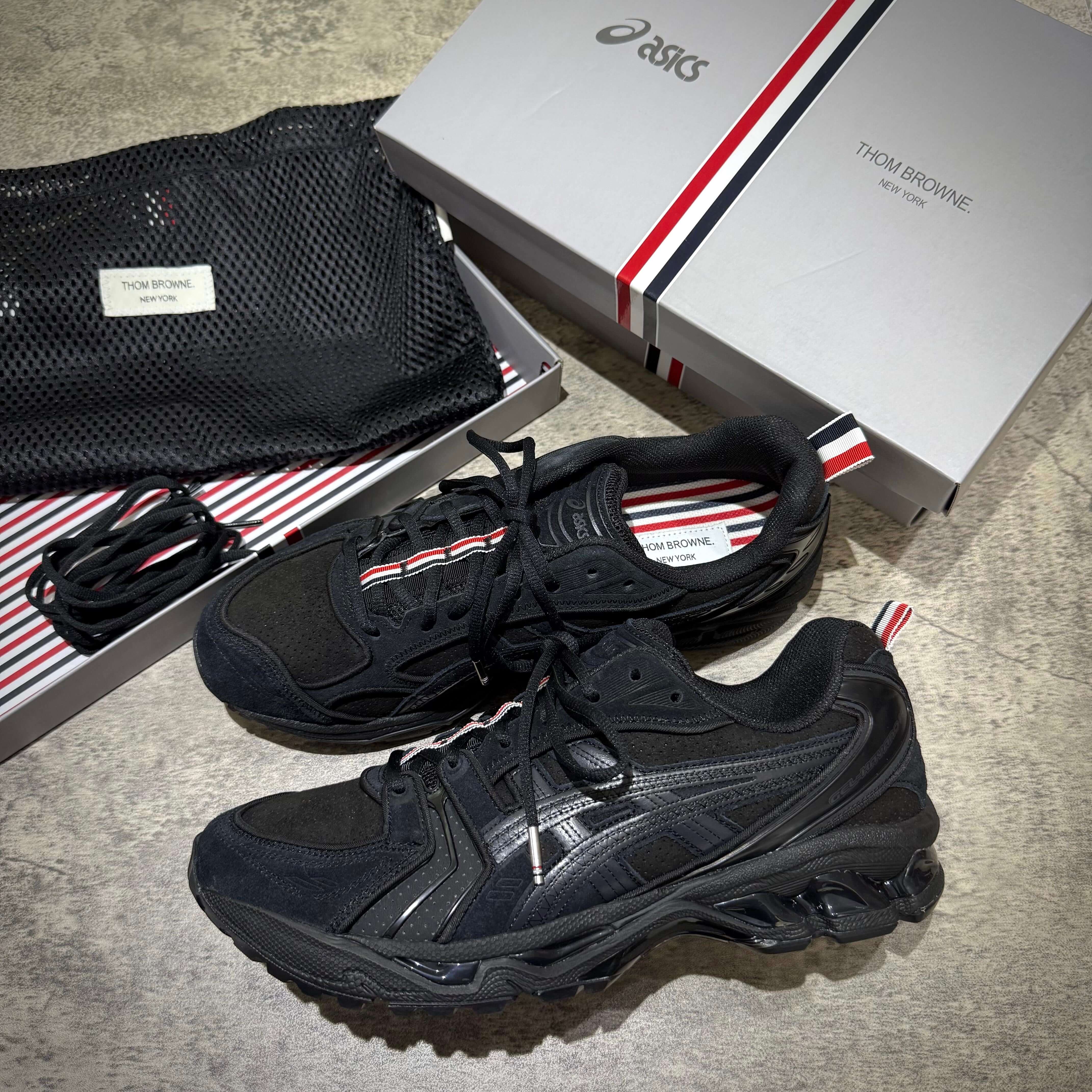 Thom Browne x Asics Gel-Kayano 14 in black, displayed with packaging and accessories, showcasing premium sneaker design.