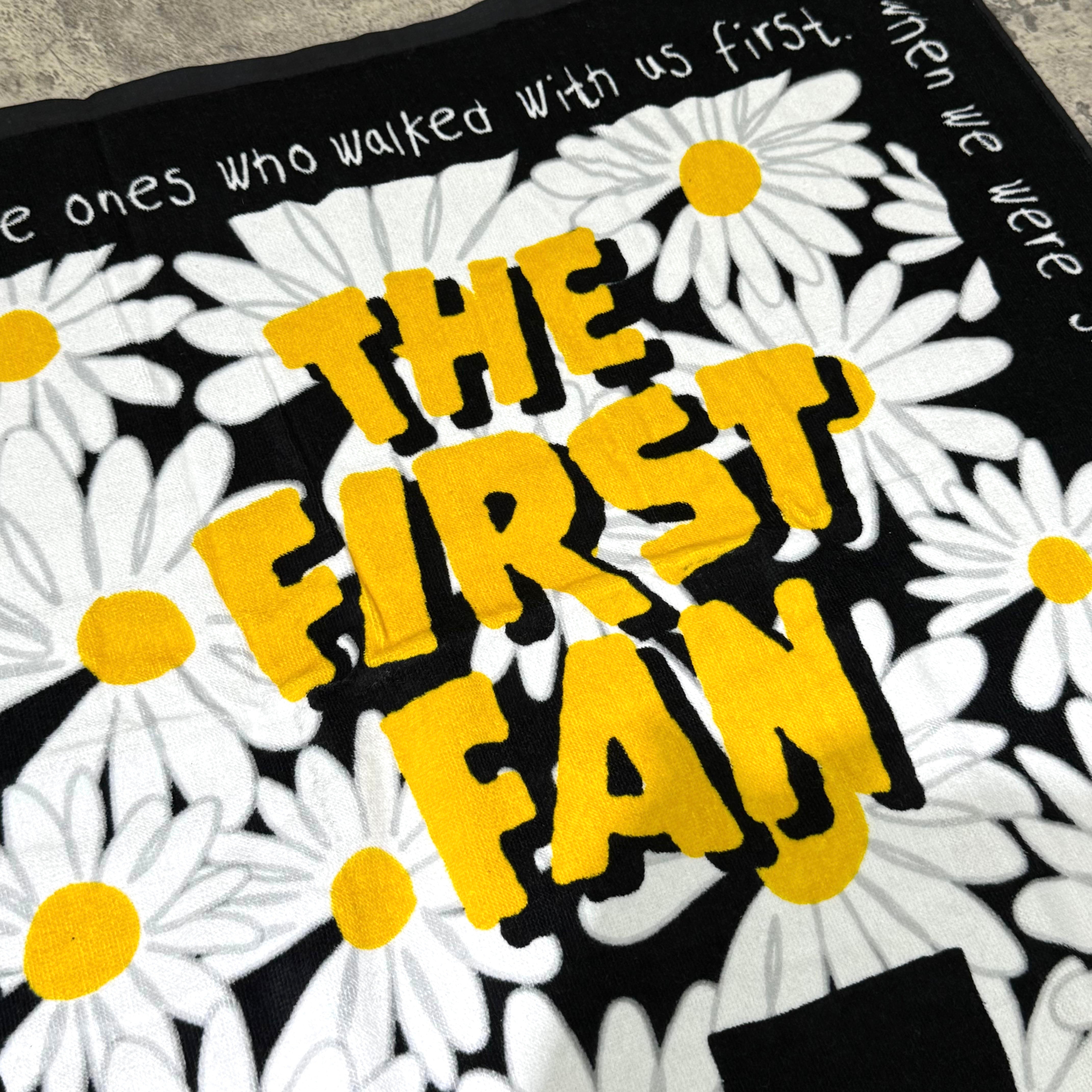 PEACEMINUSONE x Toy Story beach towel featuring 'THE FIRST FAN' design with daisies and yellow accents.