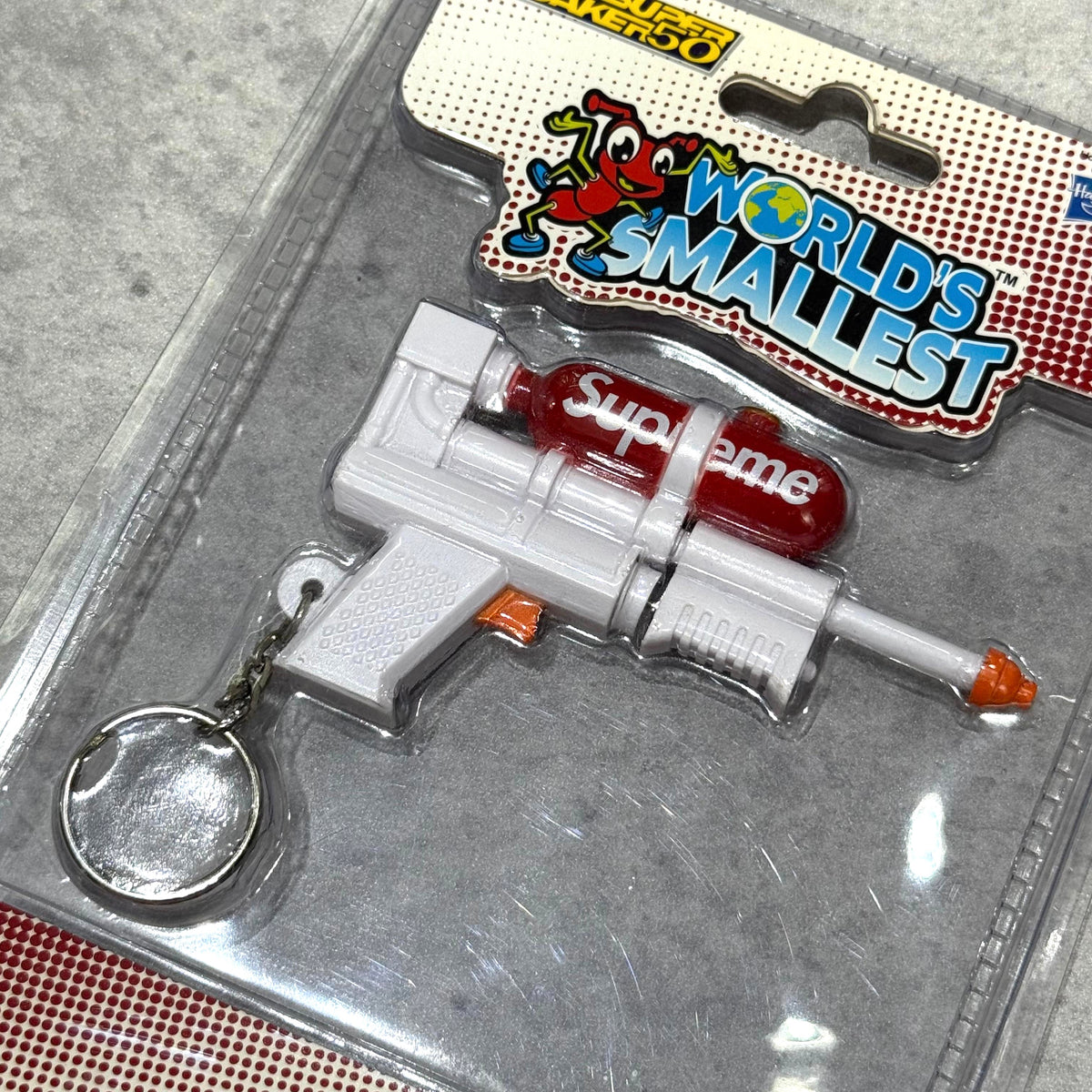 Supreme Super Soaker 50 Water Blaster Keychain in packaging, featuring a miniature water blaster design with a red canister.