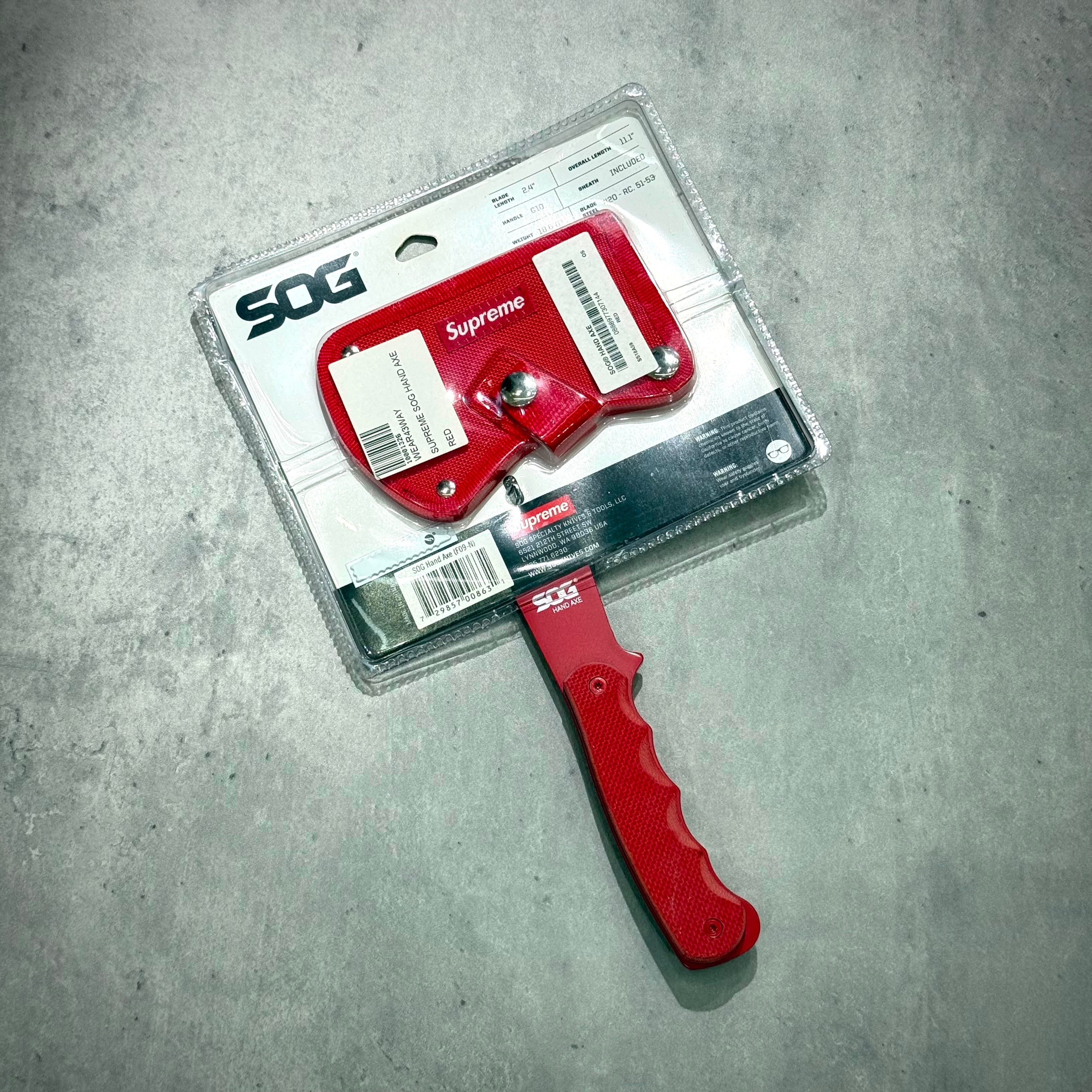 Supreme SOG Hand Axe - Red with packaging, showcasing the design and logo on the axe head.