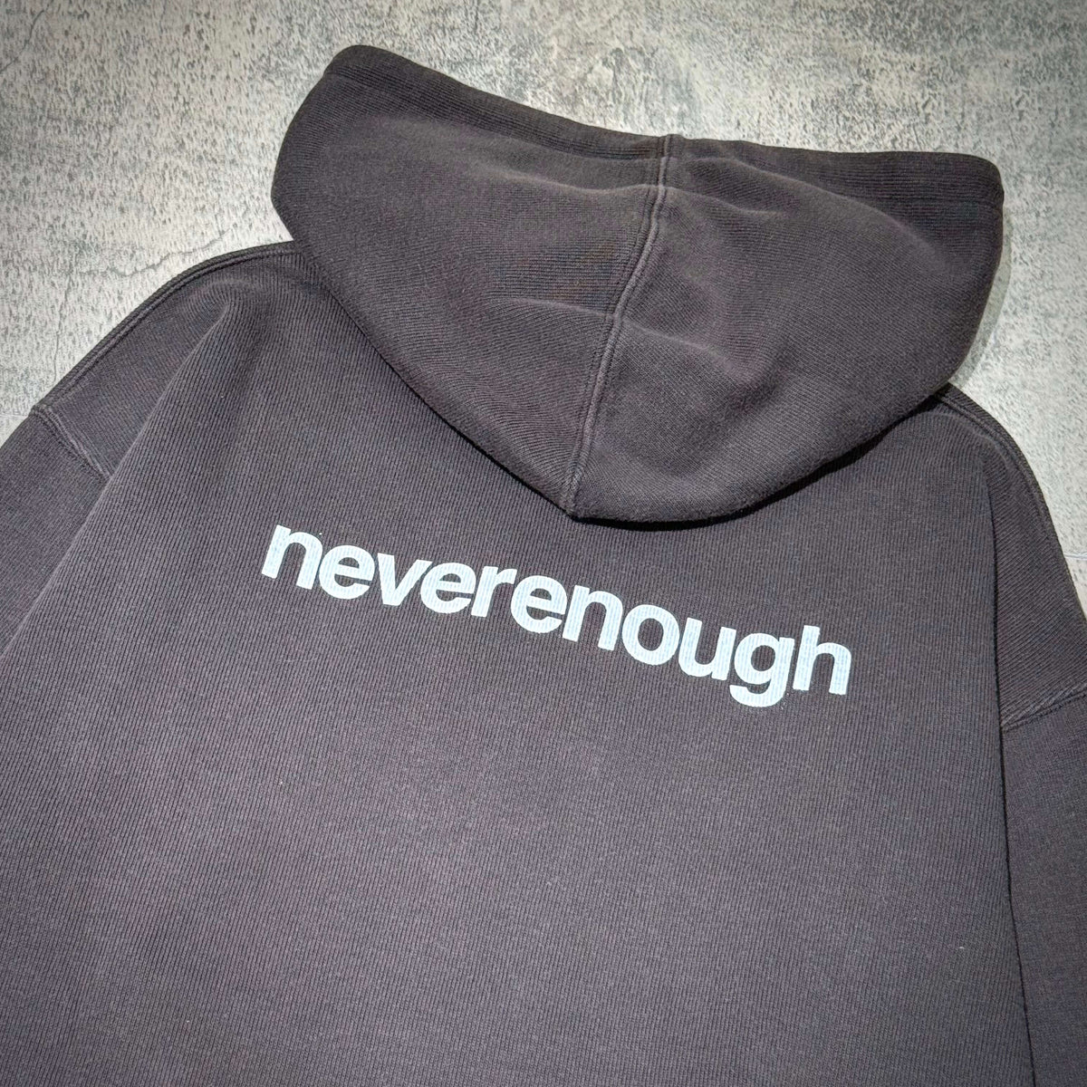 thisisneverthat x Fragment Design Hoodie - Off Black, showcasing the back with 'neverenough' text on a dark fabric.
