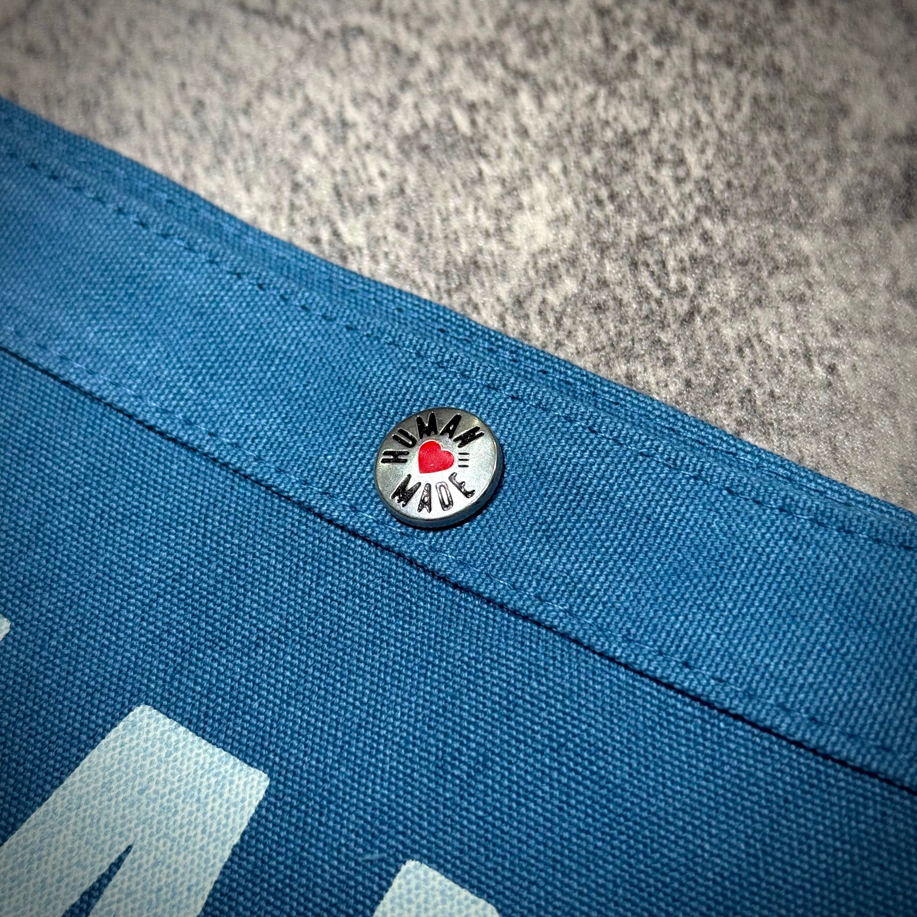 Close-up of the button detail on the Human Made Paper Boy Bag HM32GD061 in blue fabric.