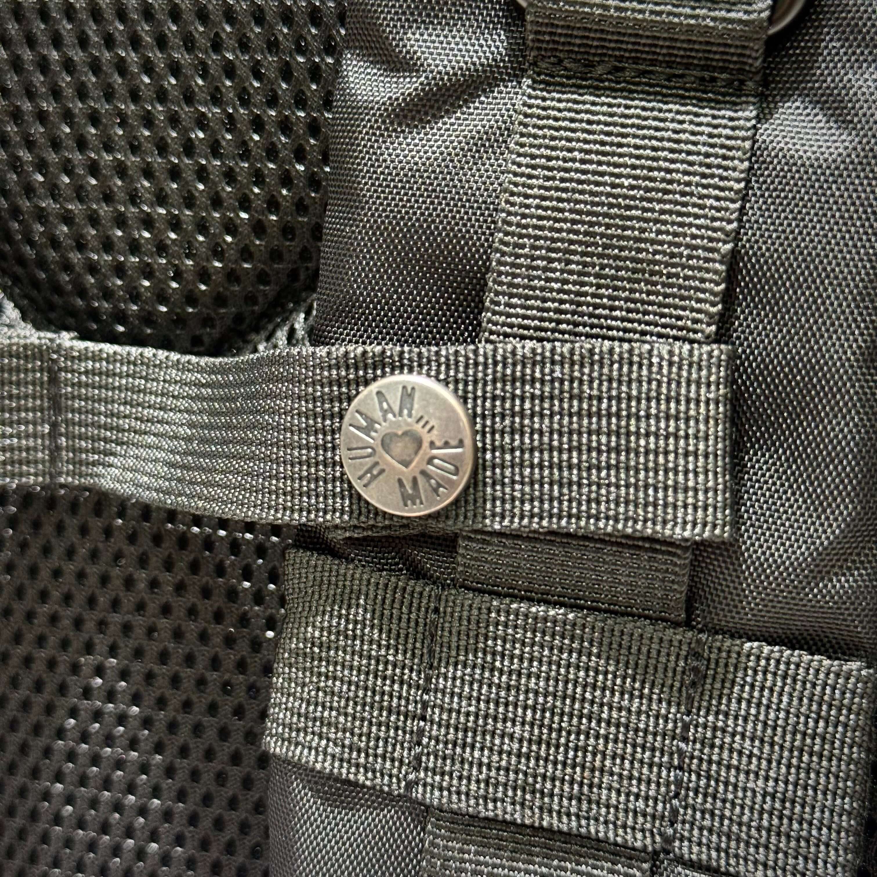 Close-up of the Human Made Military Backpack button and strap detailing showing brand emblem.