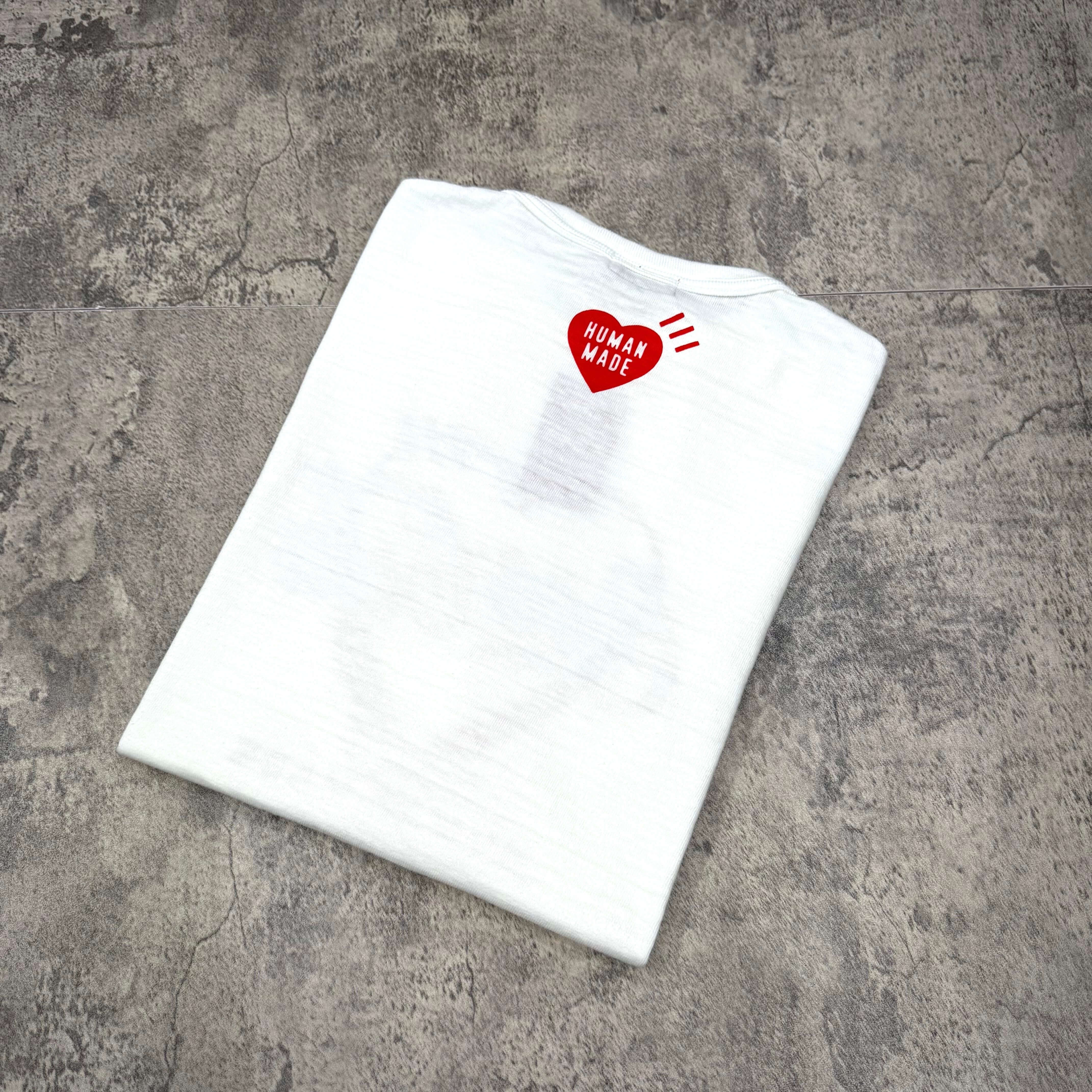 Human Made Coca Cola Graphic Tee folded on a textured background with red Human Made logo on the shoulder.