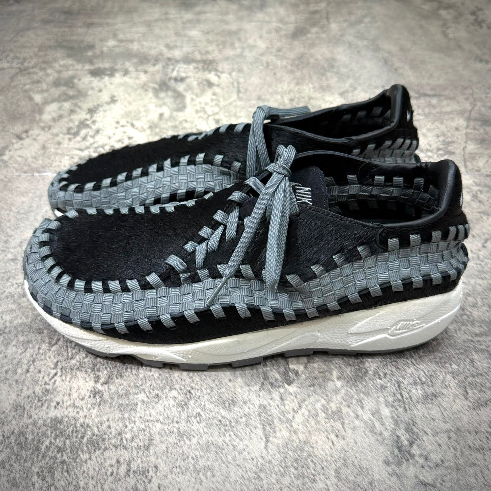 Nike Air Footscape Woven Black Smoke Grey shoes on a textured surface.