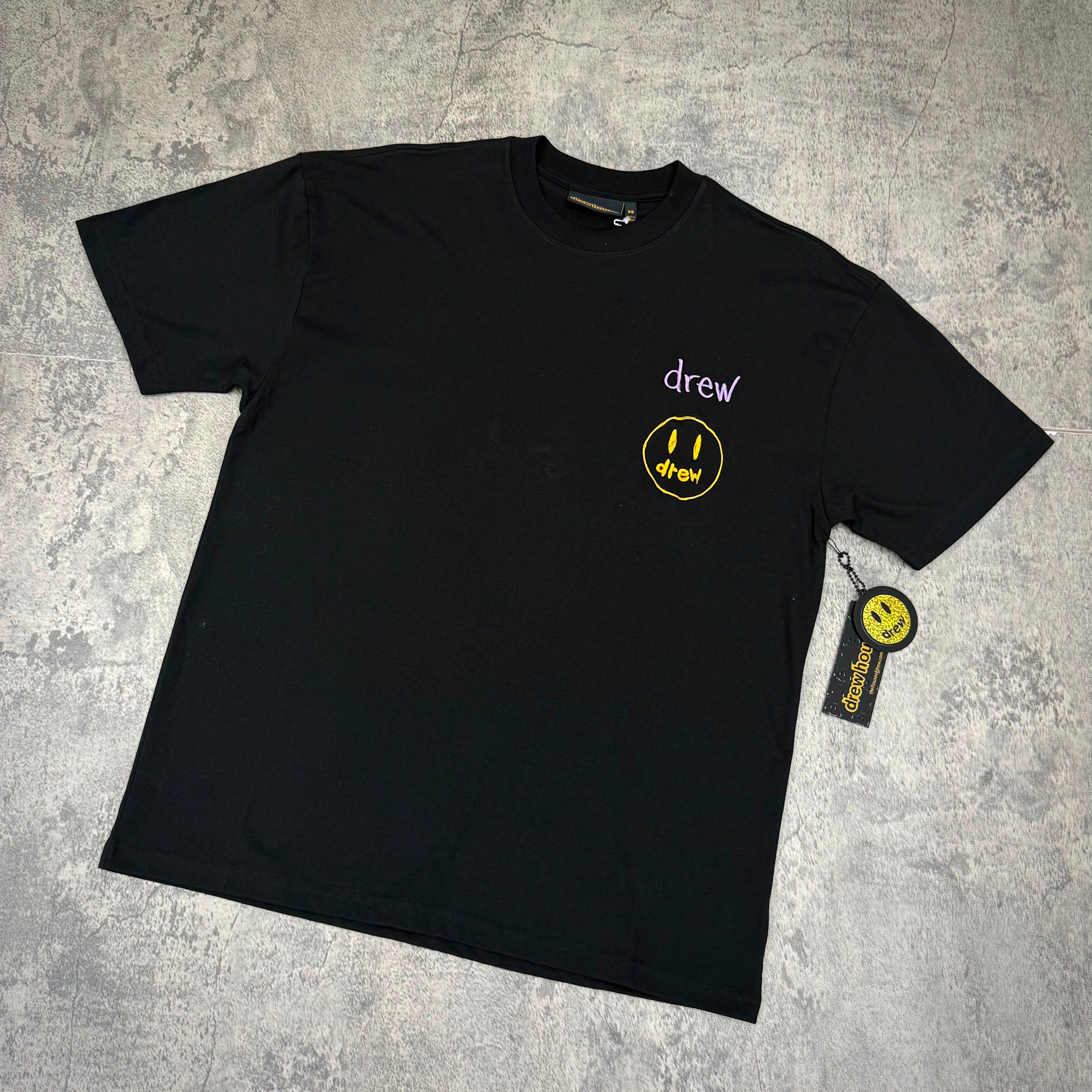 Drew House Ssense Exclusive Stacked Tee in black with yellow smiley logo and brand tag.