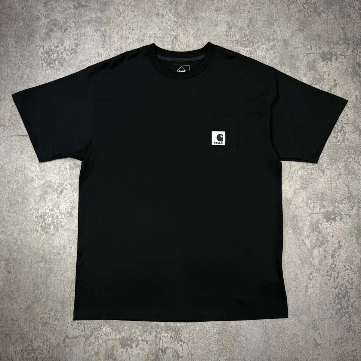 Carhartt WIP x F.C.Real Bristol Pocket Tee in black color, featuring a front pocket with logo.