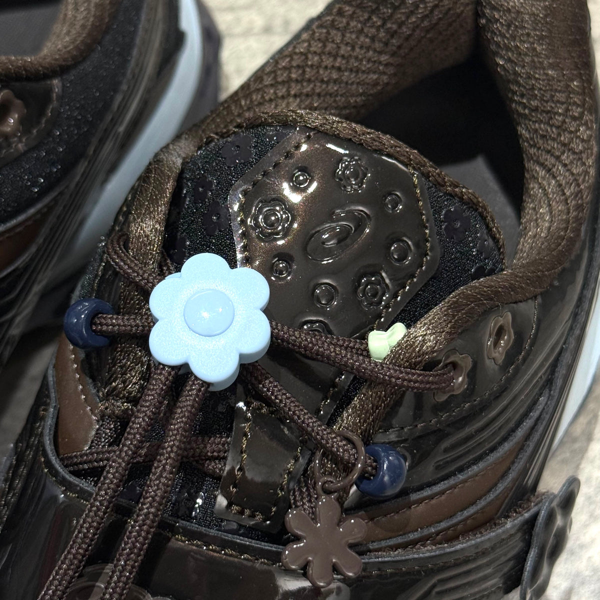 Close-up of the Cecilie Bahnsen x Asics Gel-Kinetic FR - Black Coffee 1203B171-001 with floral laces and glossy finish.
