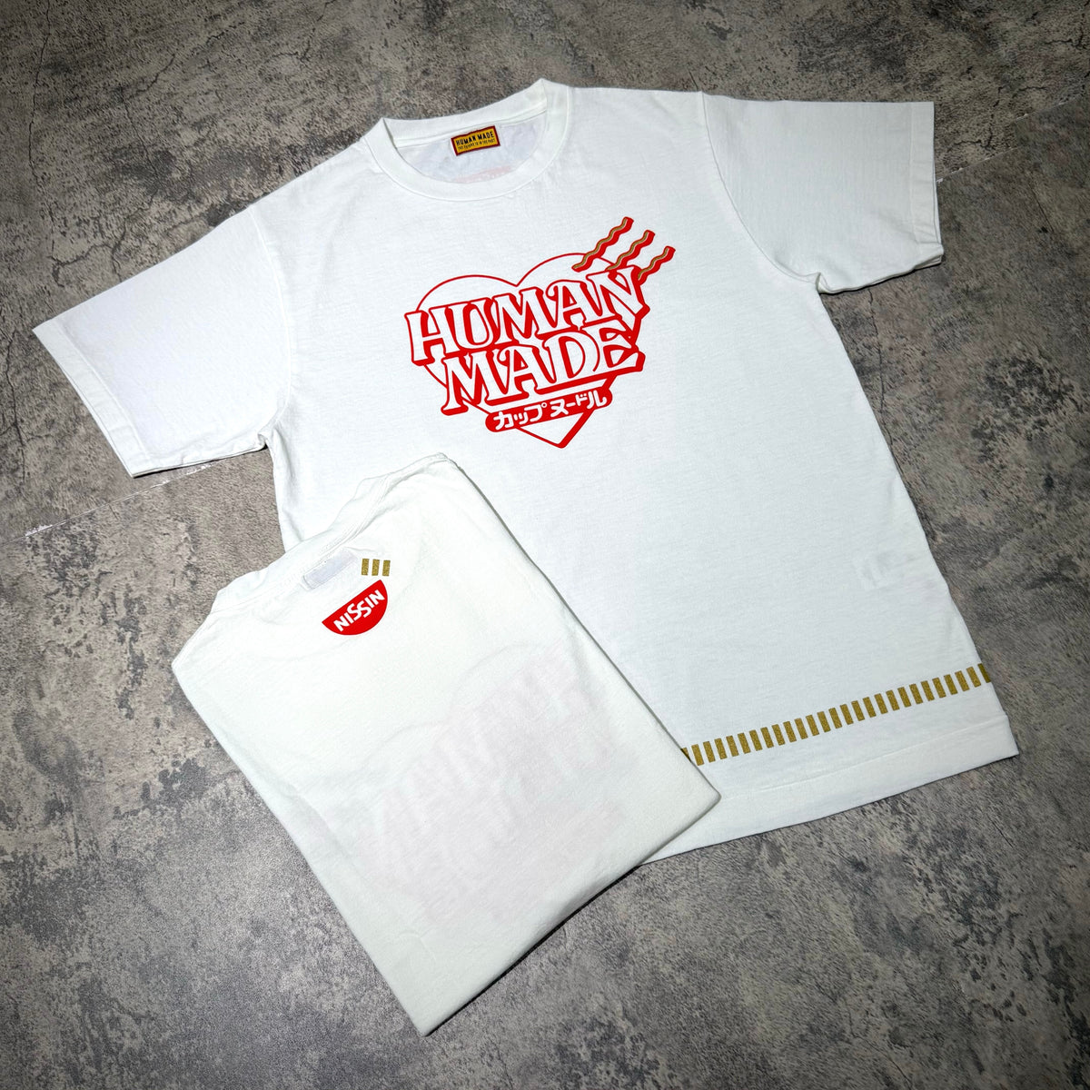 Human Made Cup Noodle Graphic Tee XX32TE002 displayed on a textured surface with another tee.