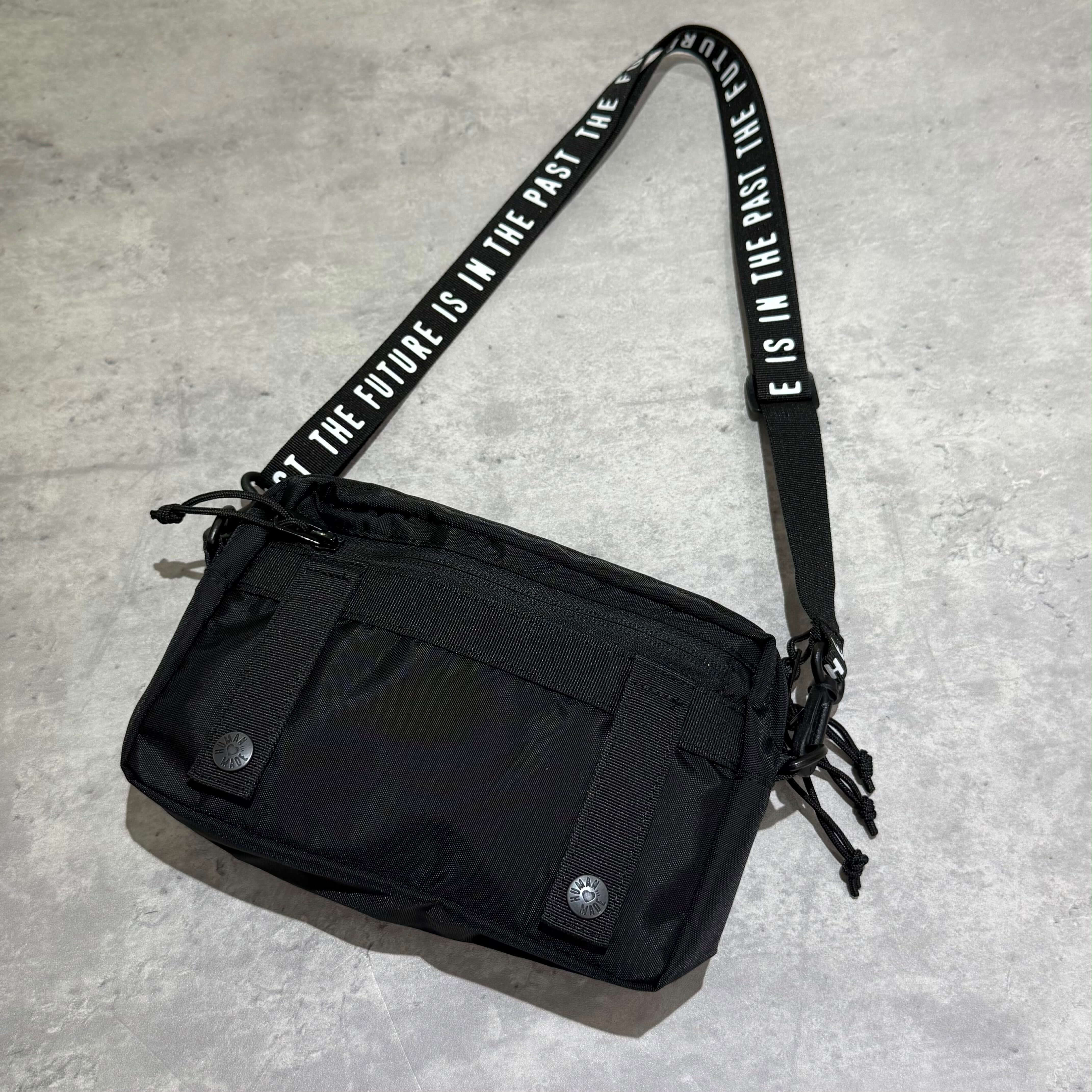 Human Made Military Pouch with adjustable strap and multiple pockets on a gray background.