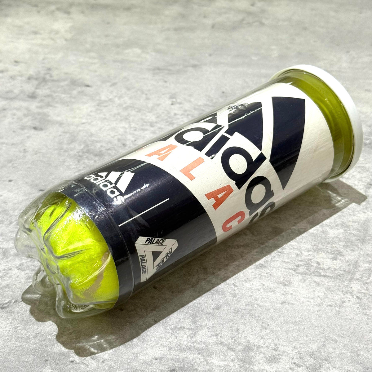 Palace x adidas Tennis Balls in a clear container on a textured surface.