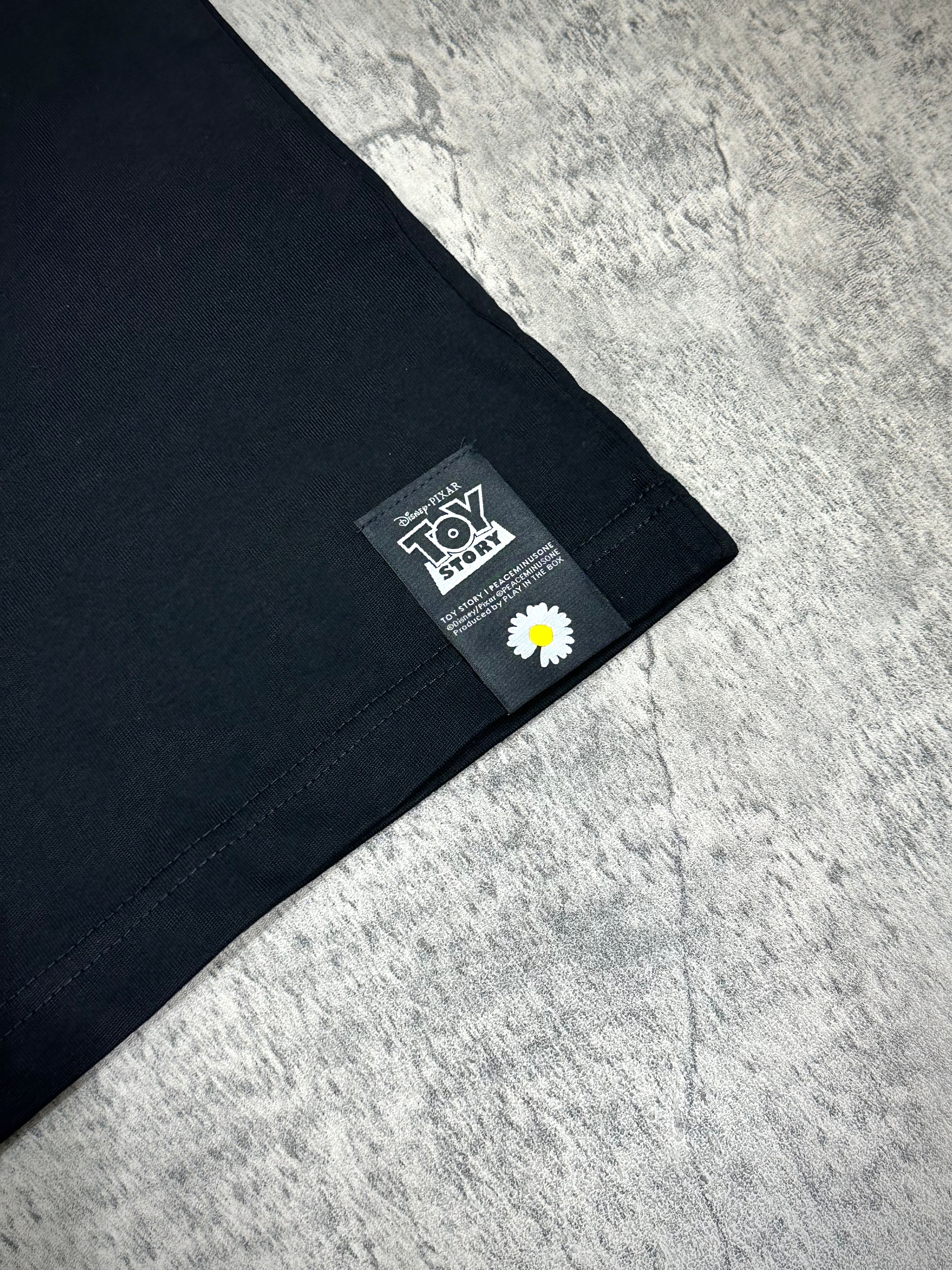 Close-up of PEACEMINUSONE x Toy Story T-shirt label with logo featuring a flower.