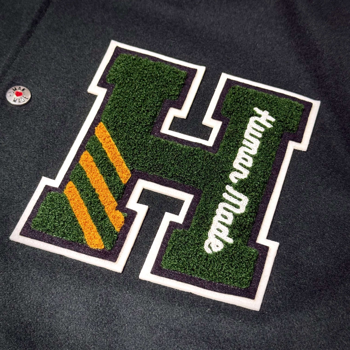 HUMAN HOPE Varsity Jacket HUMAN MADE x j-hope of BTS featuring green and yellow embroidered logo detail.