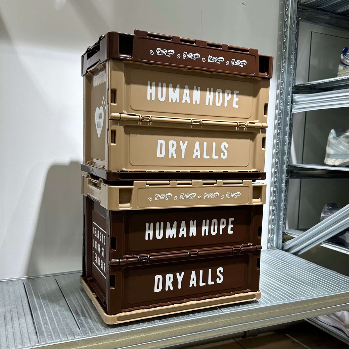 Stack of Human Hope Container 20L in brown and beige, labeled 'DRY ALLS' on shelves.