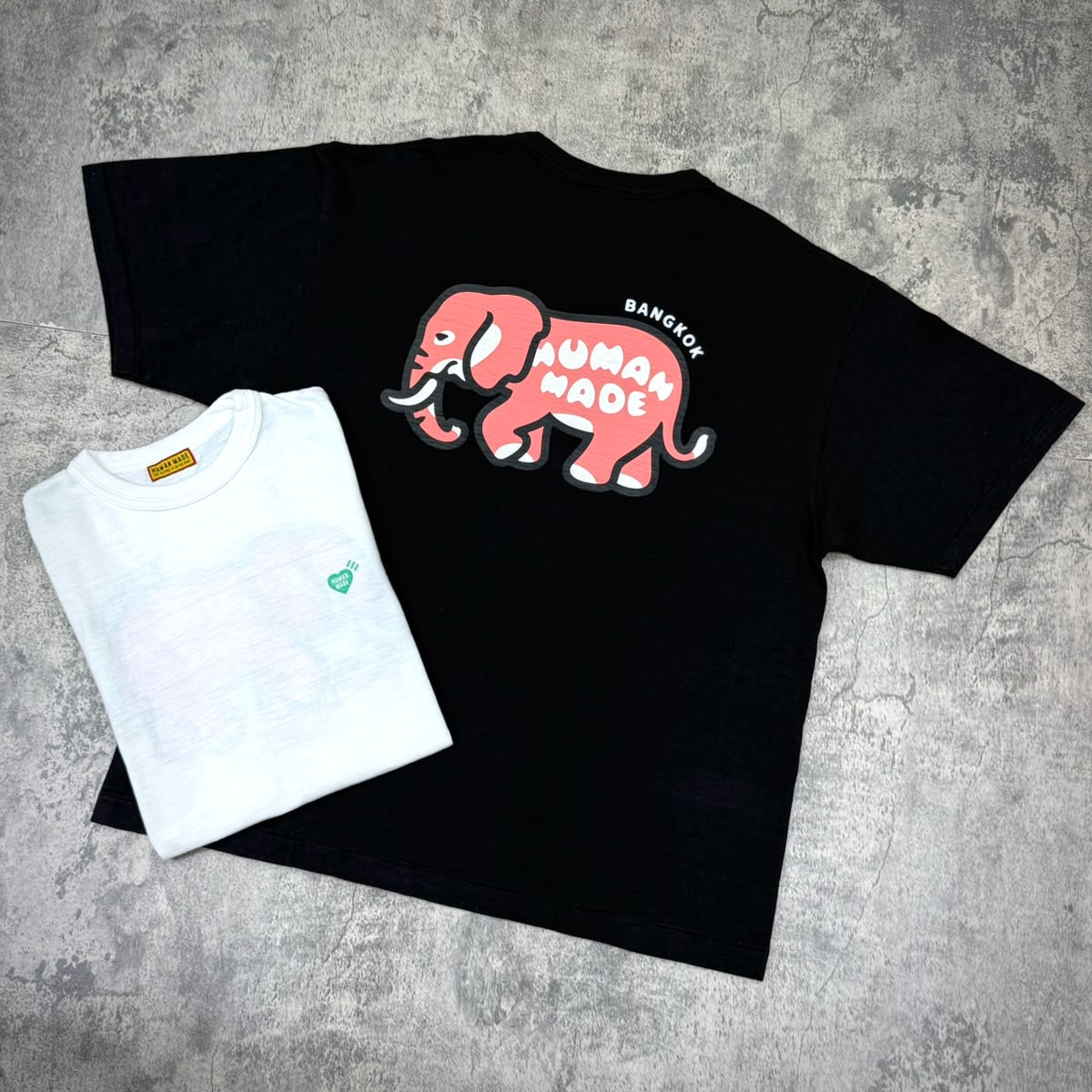 Human Made Bangkok Exclusive Elephant Back Logo Tee displayed with a white shirt underneath on a textured background.