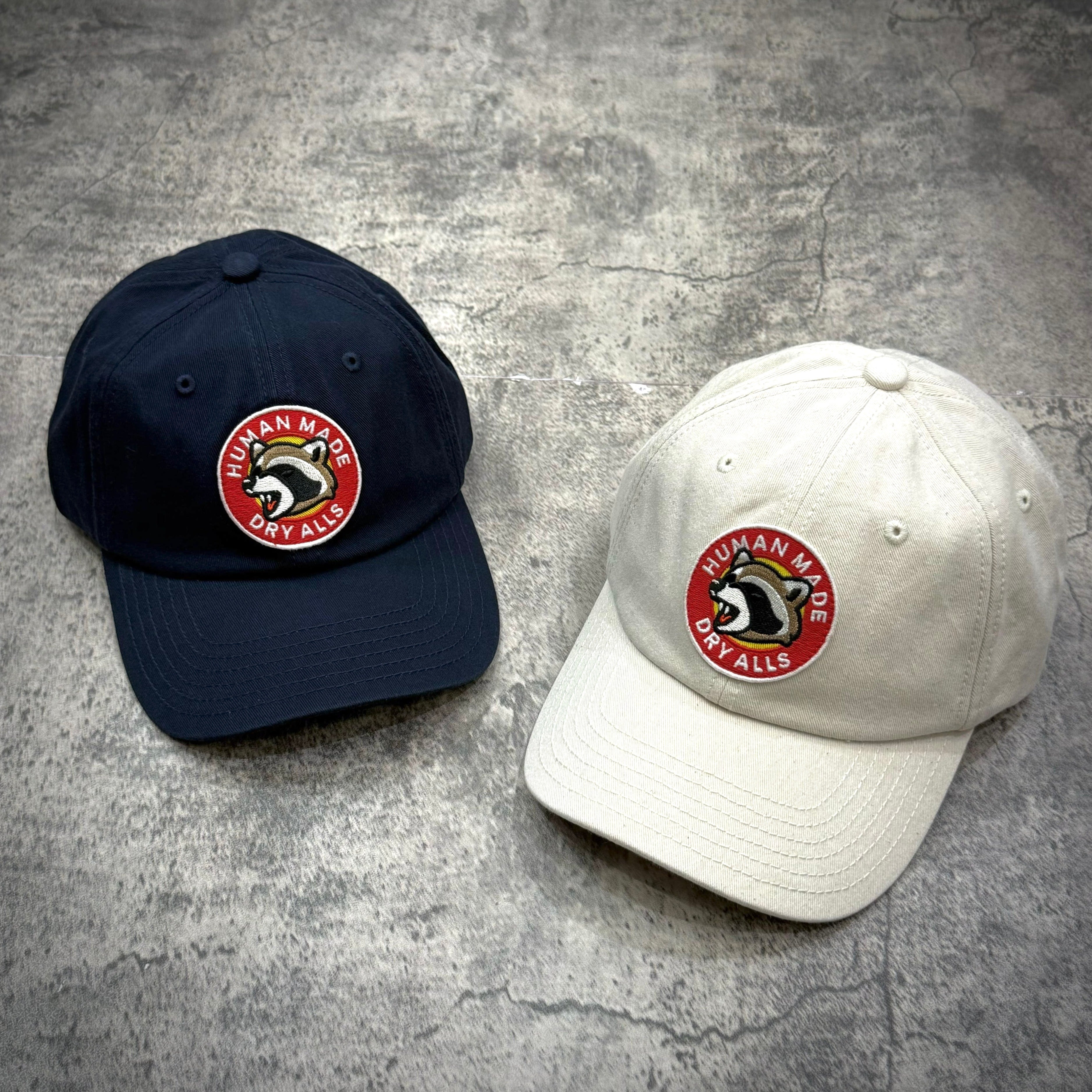 Human Made Jamsil Exclusive 6 Panel Twill Raccon Cap in navy and white color options on a textured background