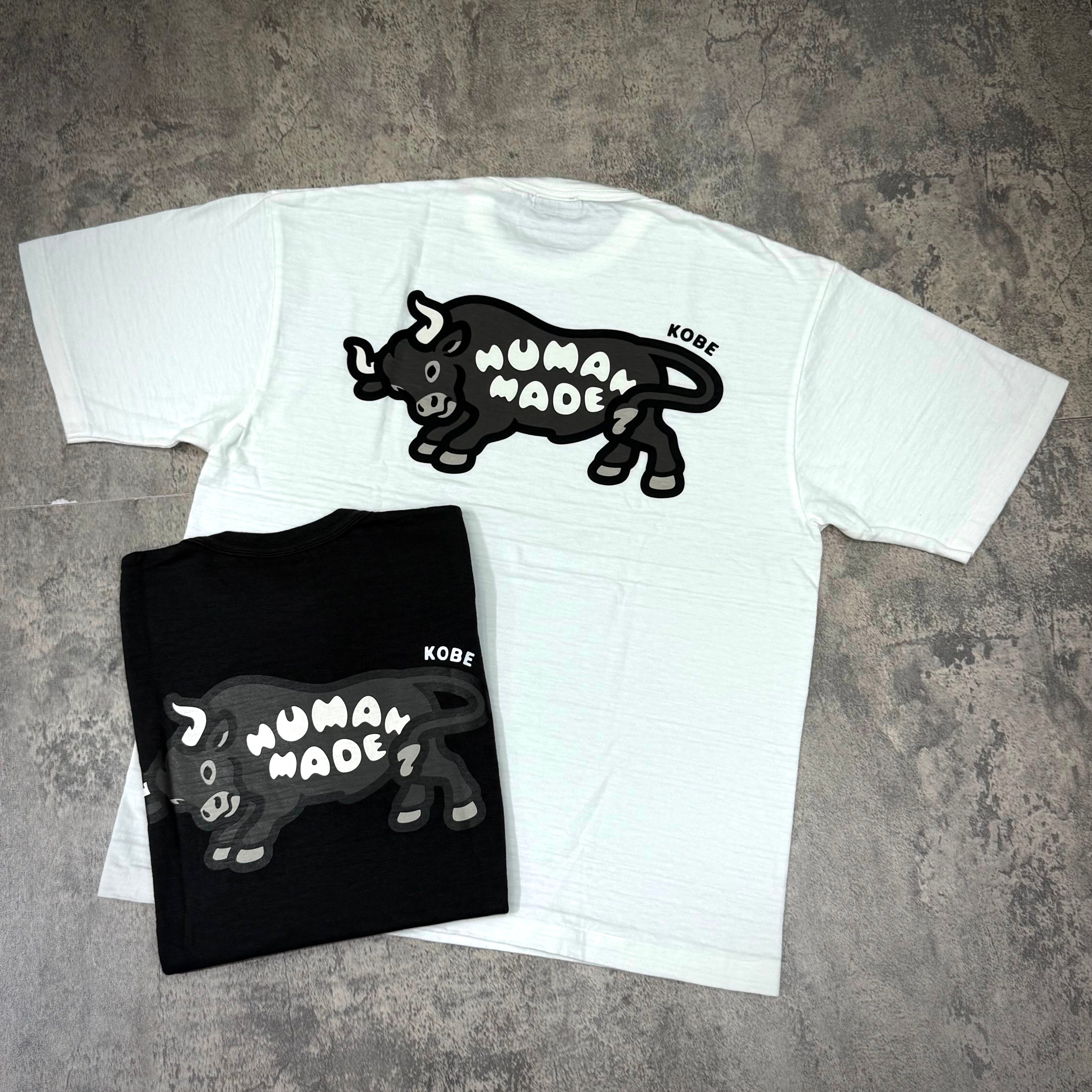 Human Made Kobe Exclusive Bull Back Logo Tee displayed in white and black colors on a textured surface.