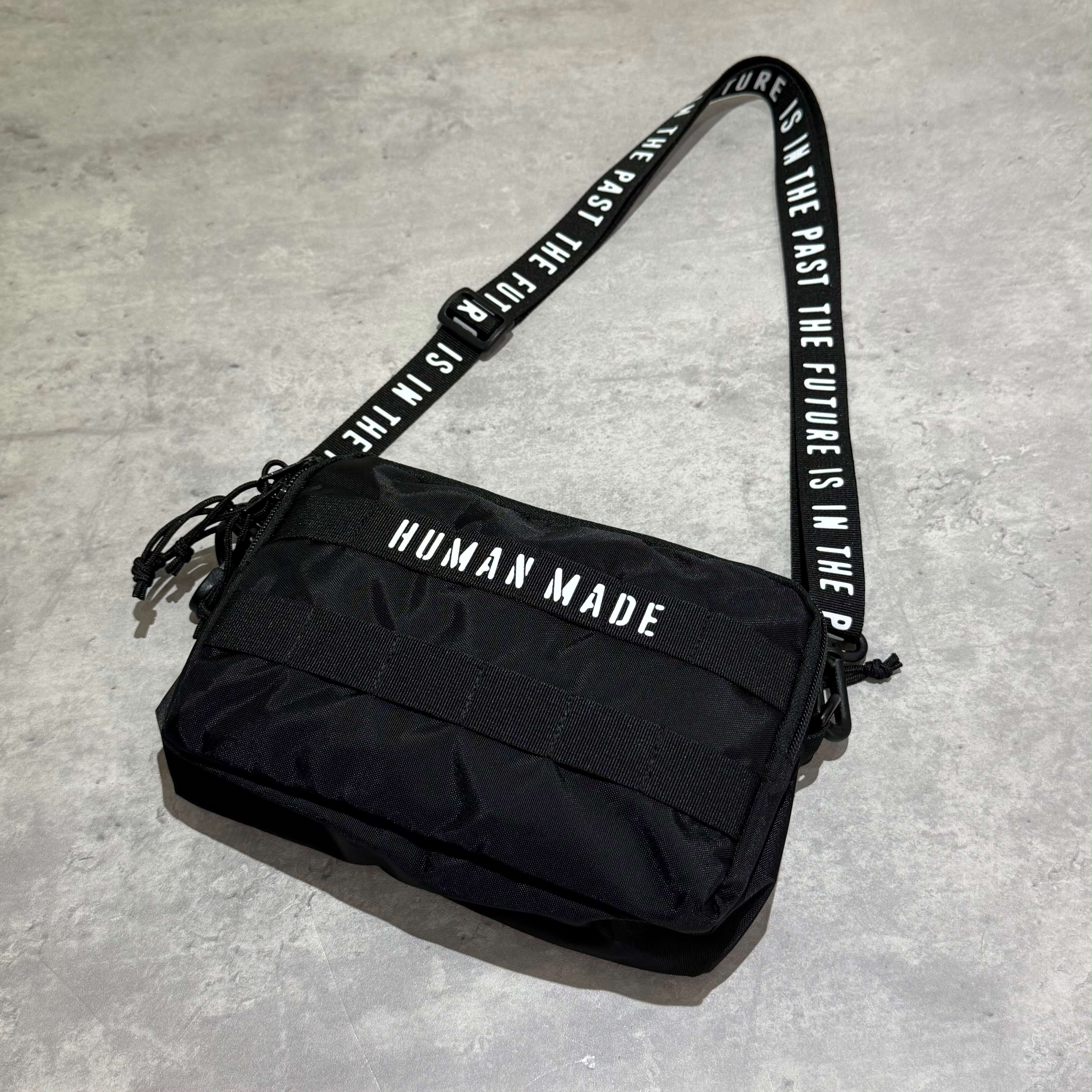 Human Made Military Pouch displayed on a gray surface, featuring a stylish black design and adjustable strap.