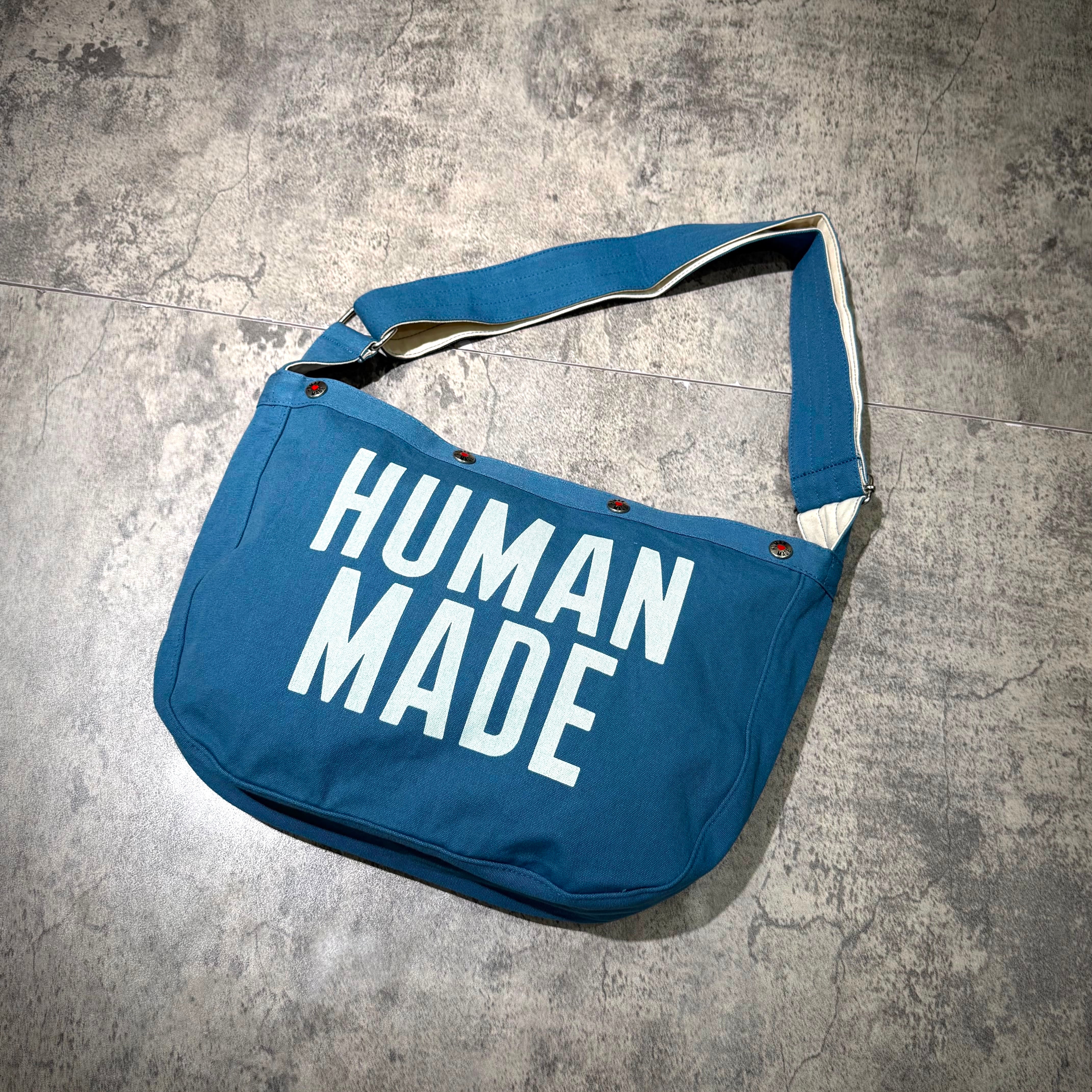 Human Made Paper Boy Bag HM32GD061 in blue with bold white text, stylish and functional design for everyday use.
