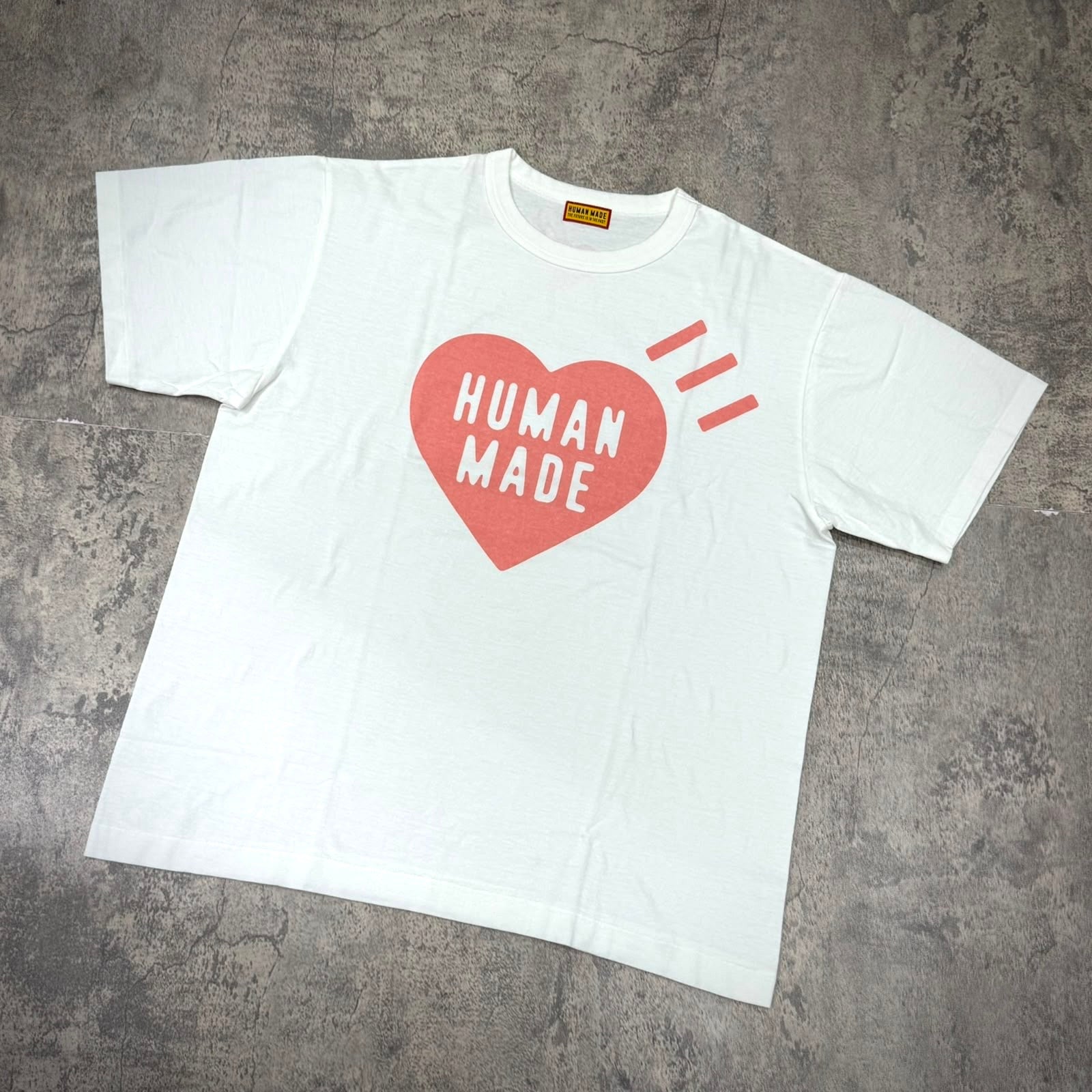 Human Made Seoul Exclusive Heart Logo Tee displayed on a grey floor, featuring a bold heart and text design.