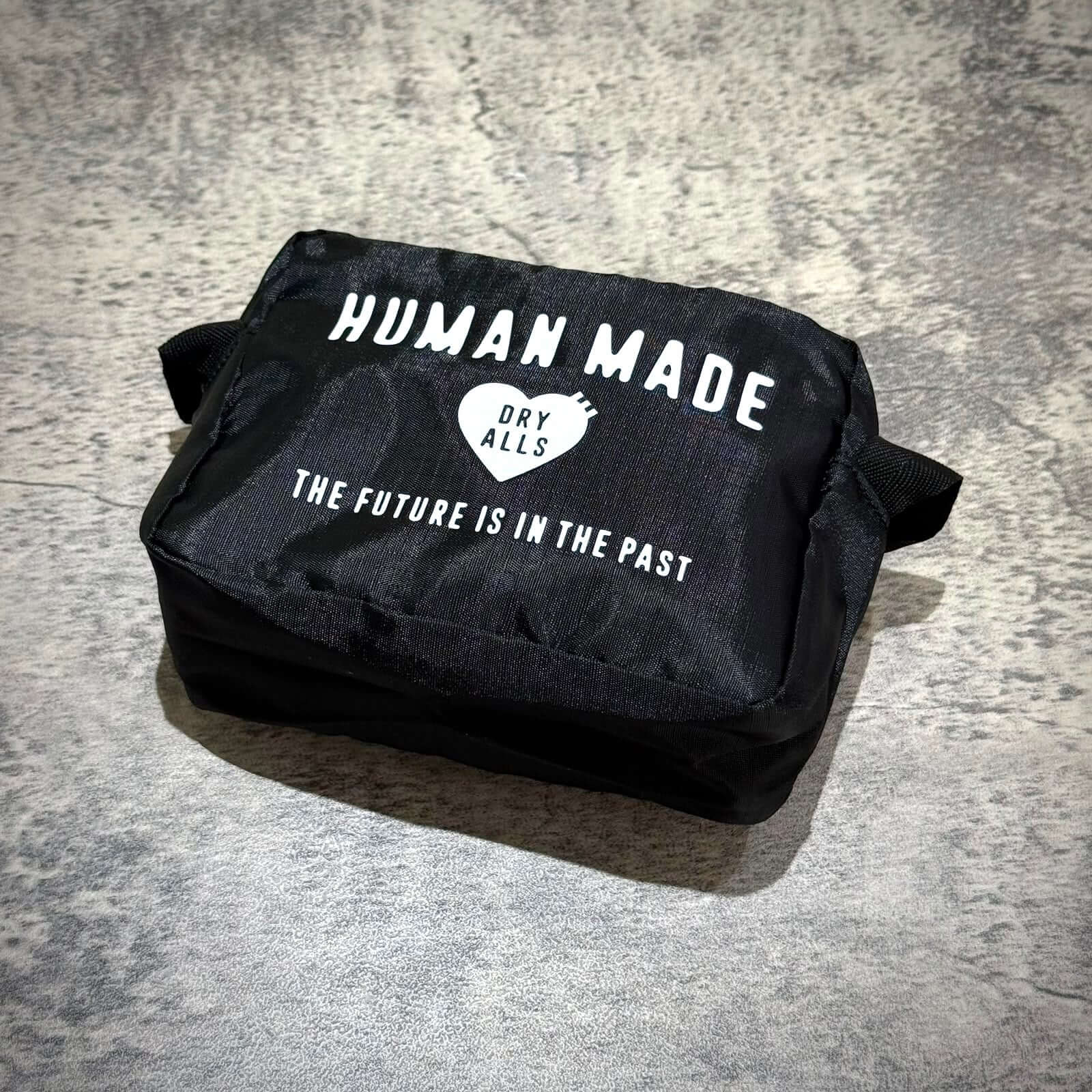 Human Made Travel Pouch displayed on a textured surface with a sleek black design and bold white text.