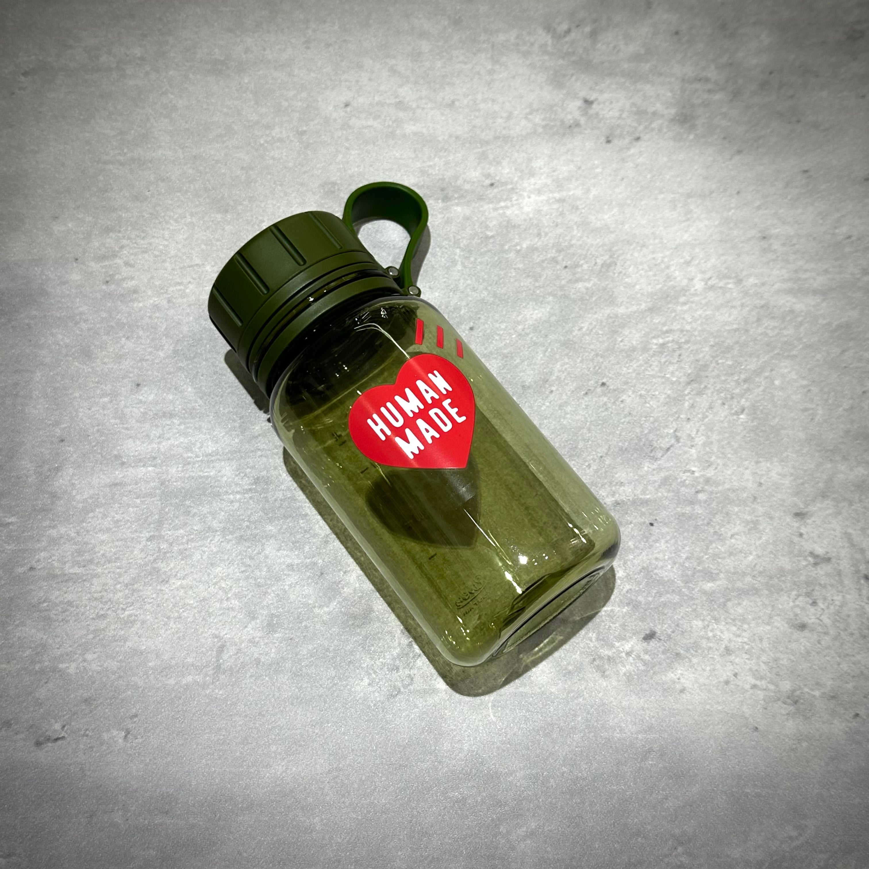 Human Made Water Bottle in green color with logo and attached handle on a gray surface.