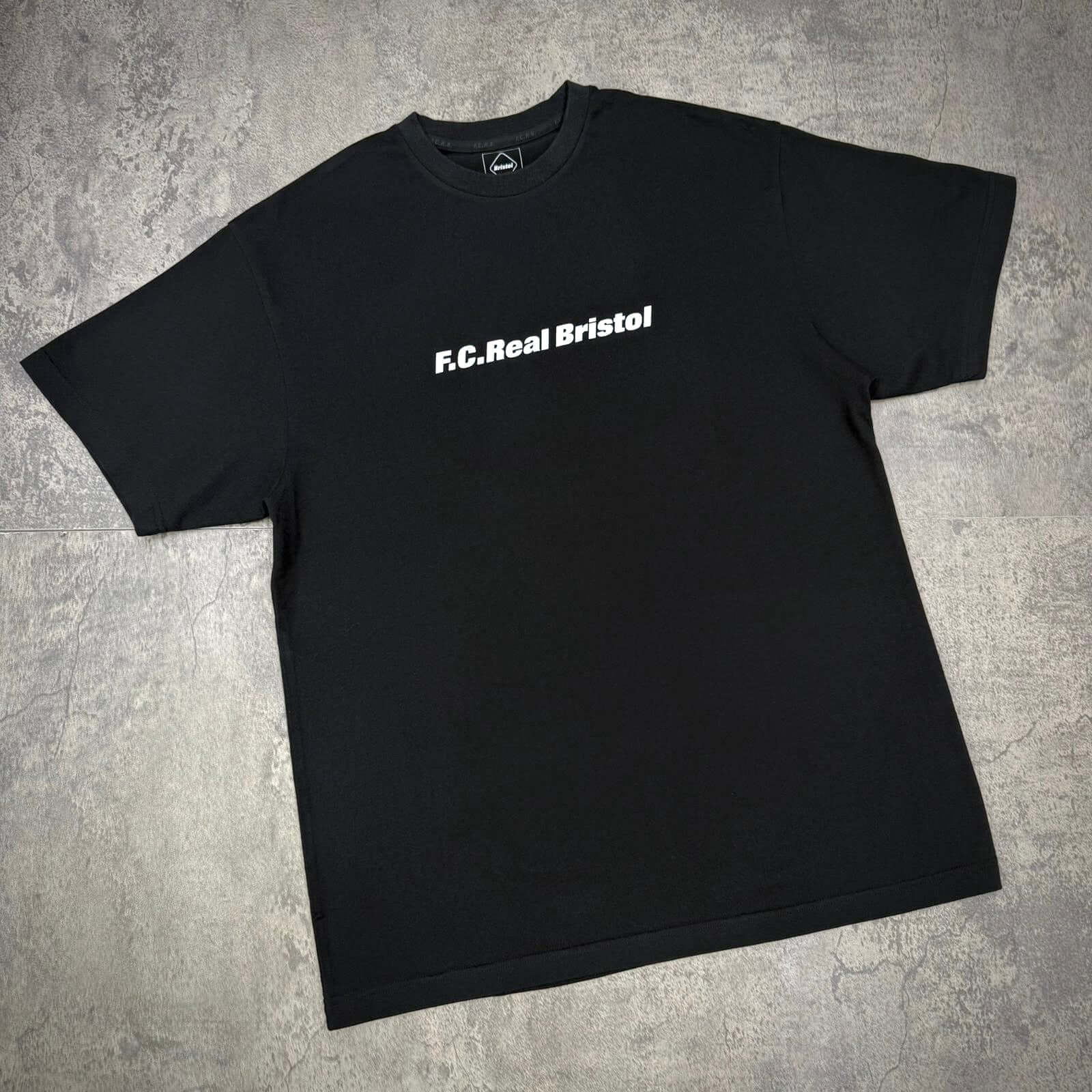 Kojiro Hyuga x FCRB On The Back Tee featuring black design with F.C. Real Bristol printed on the front.